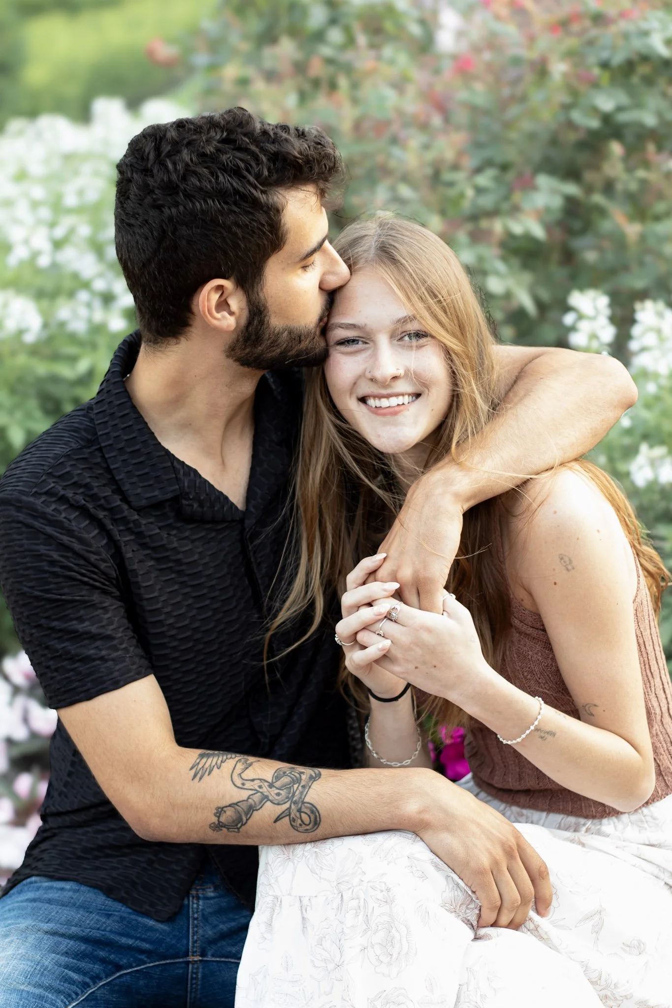 A couple sharing an affectionate moment outdoors, with the man kissing the woman on the forehead while she smiles.
