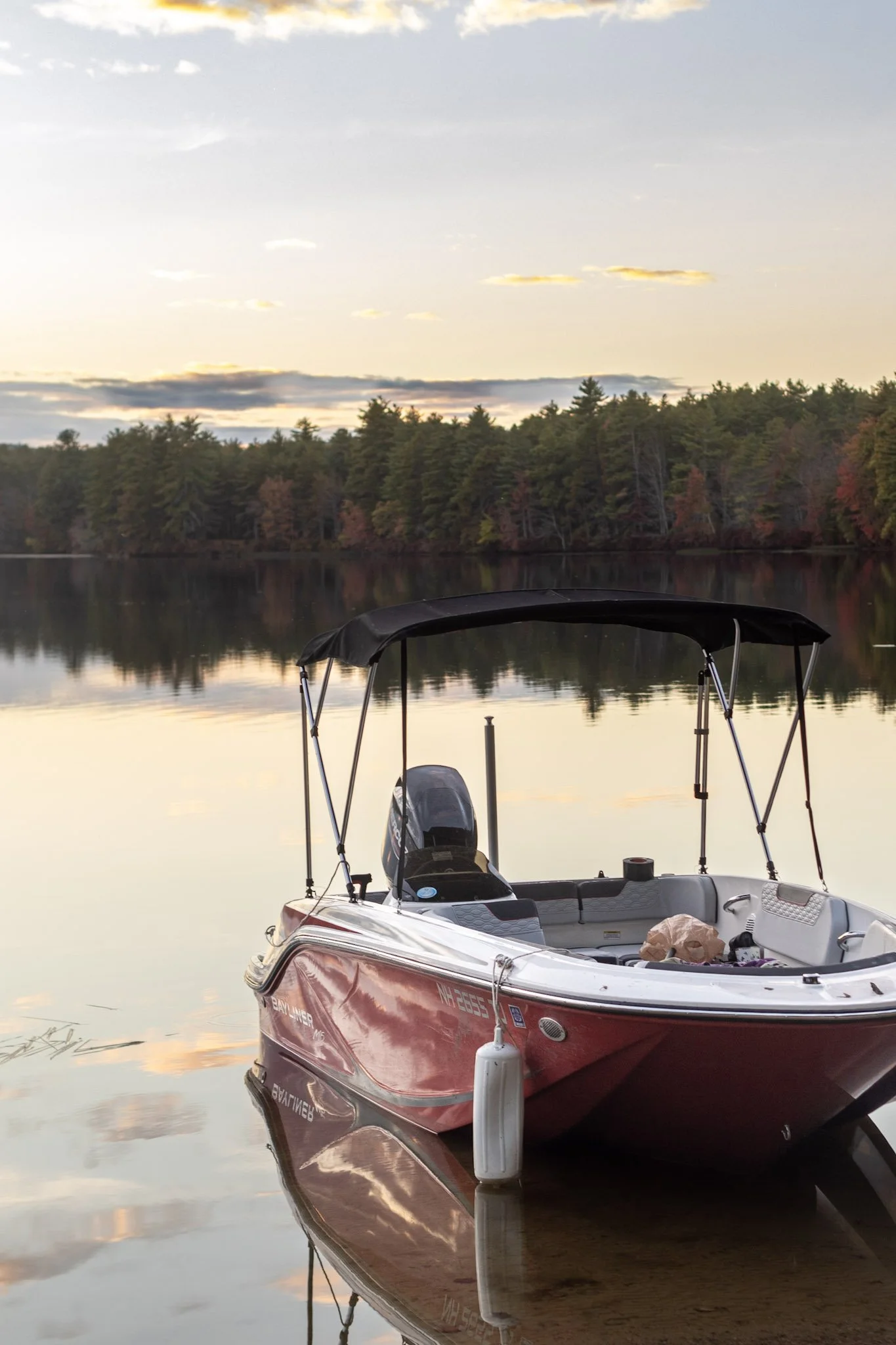A red motorboat docked at a calm lake with a forest in the background at sunset.