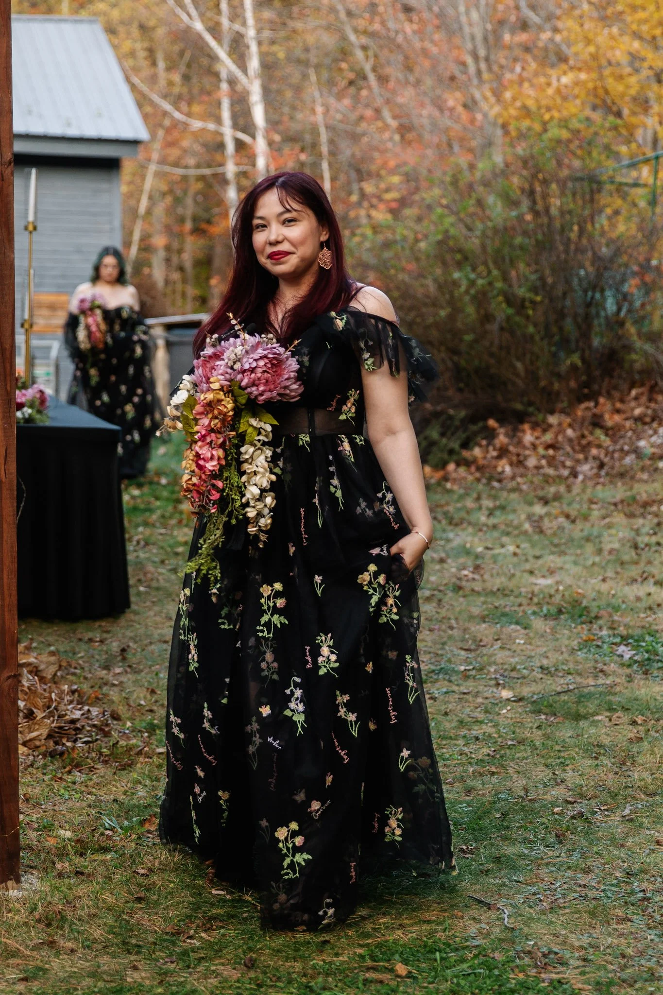 Woman in a black floral dress holding a bouquet of flowers outdoors during fall.
