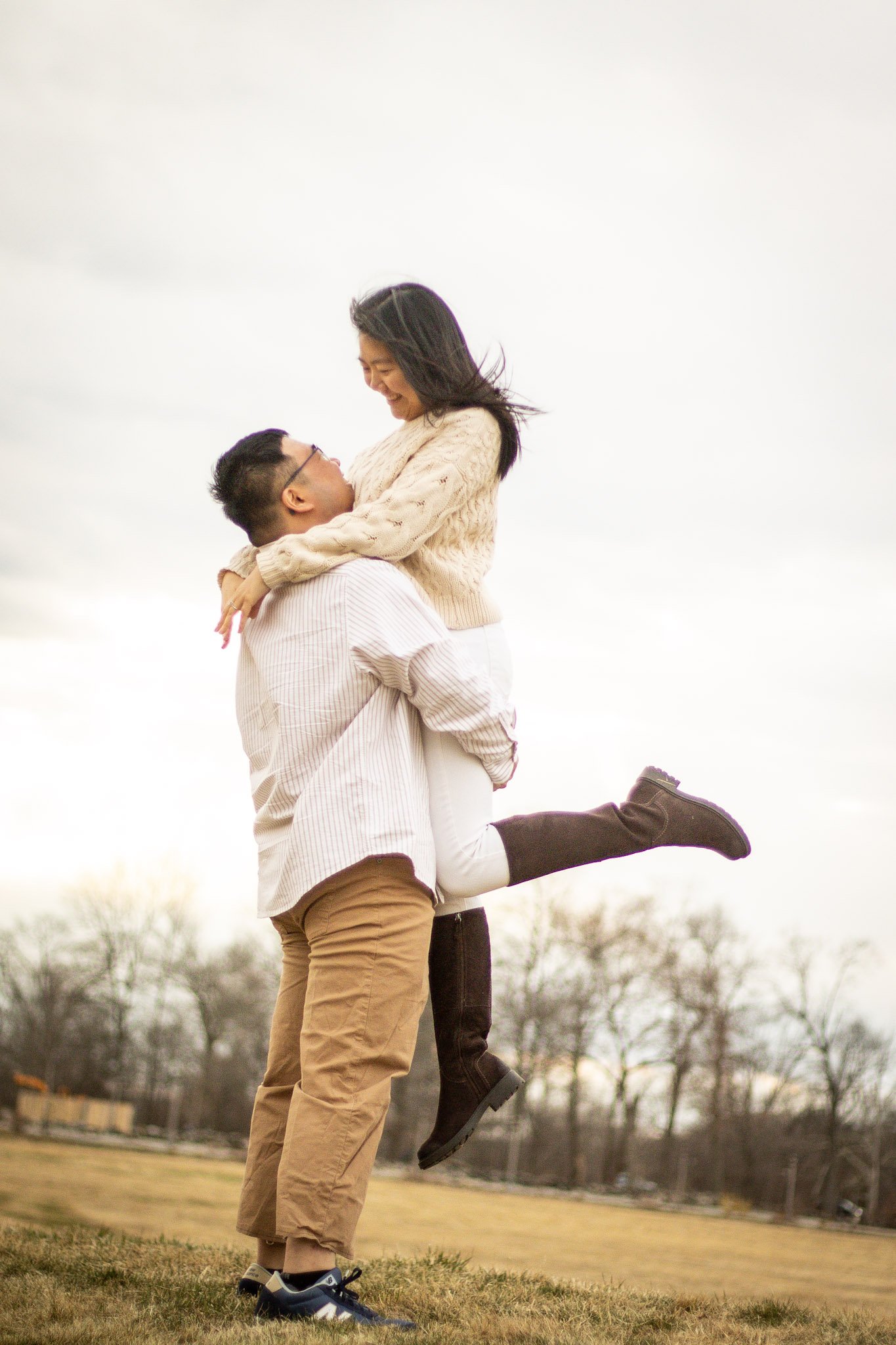 A man lifting a woman off the ground in an outdoor park during the daytime, both smiling and enjoying each other's company.