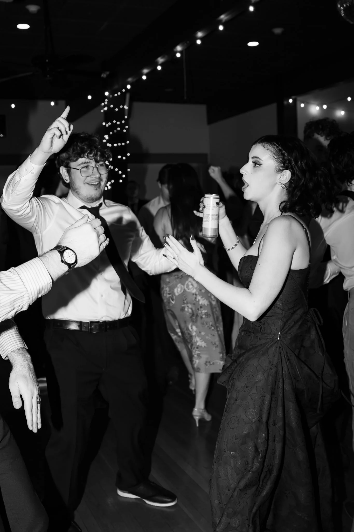 People dancing at a party or celebration with string lights overhead, black and white photo.
