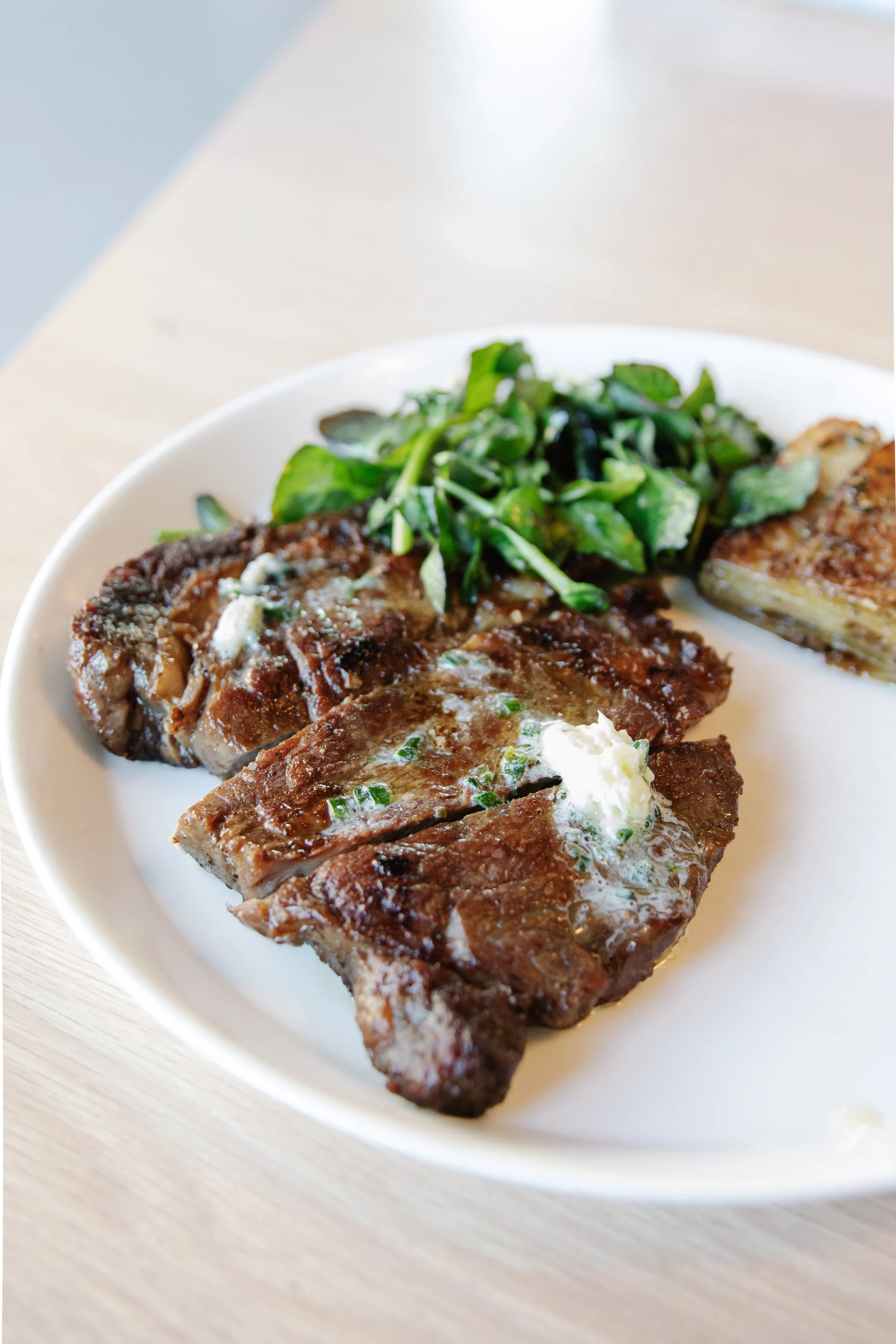 Slices of cooked meatloaf with a pat of butter and chopped herbs on top, served with a side of salad greens on a white plate.