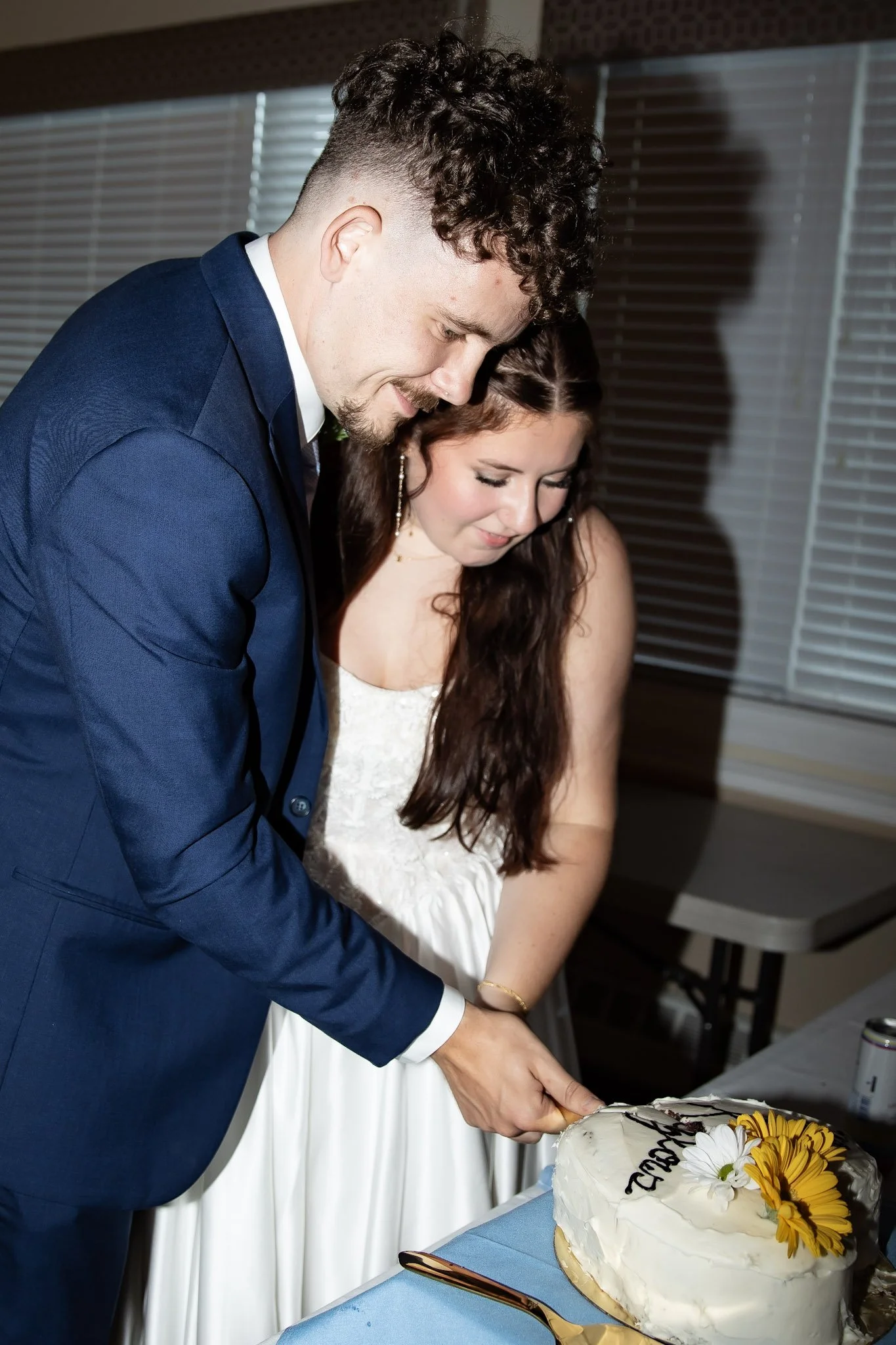 A couple, dressed in formal attire, cutting a wedding cake together at a celebration.