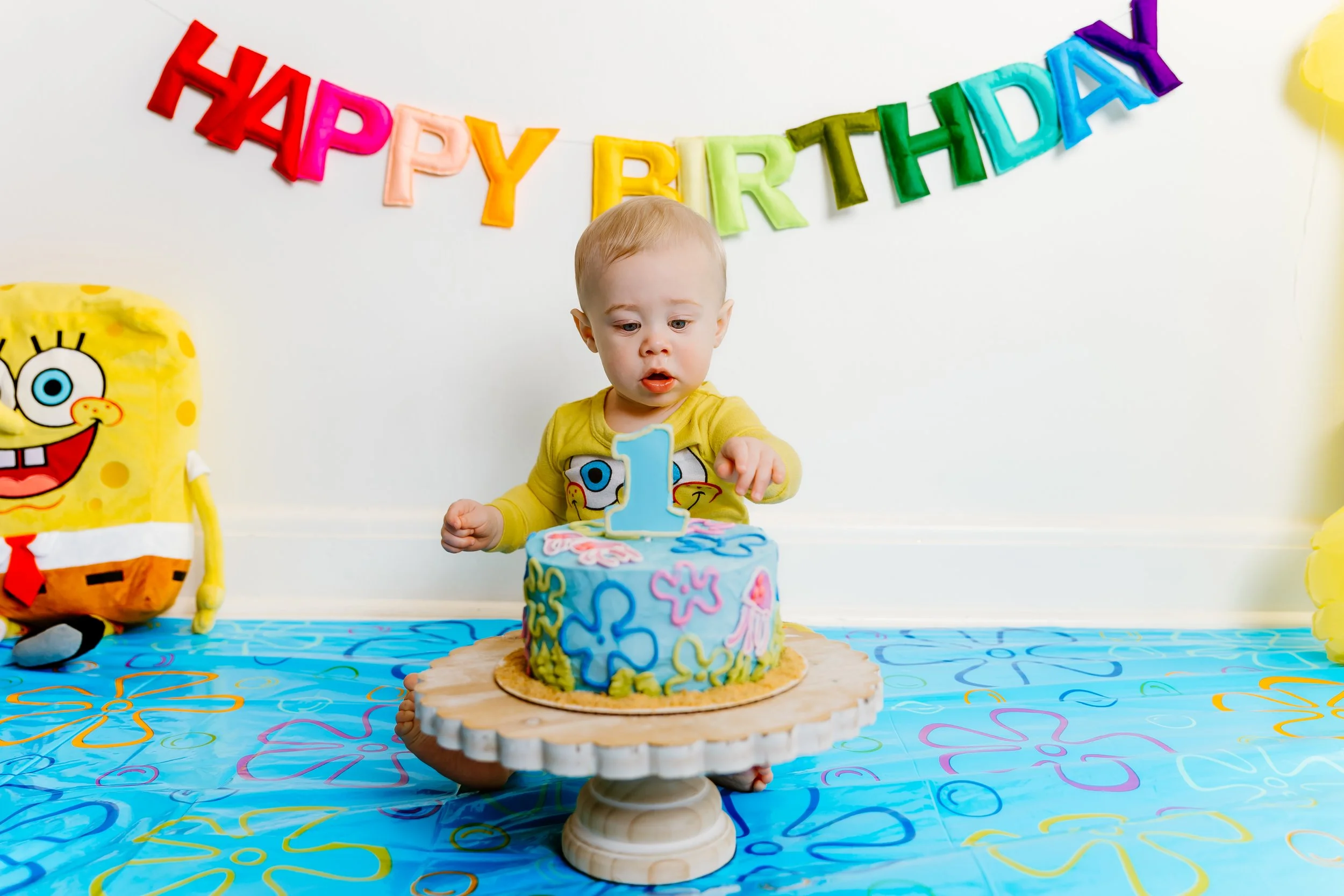 Toddler sitting with birthday banner and number one balloon during cake smash session