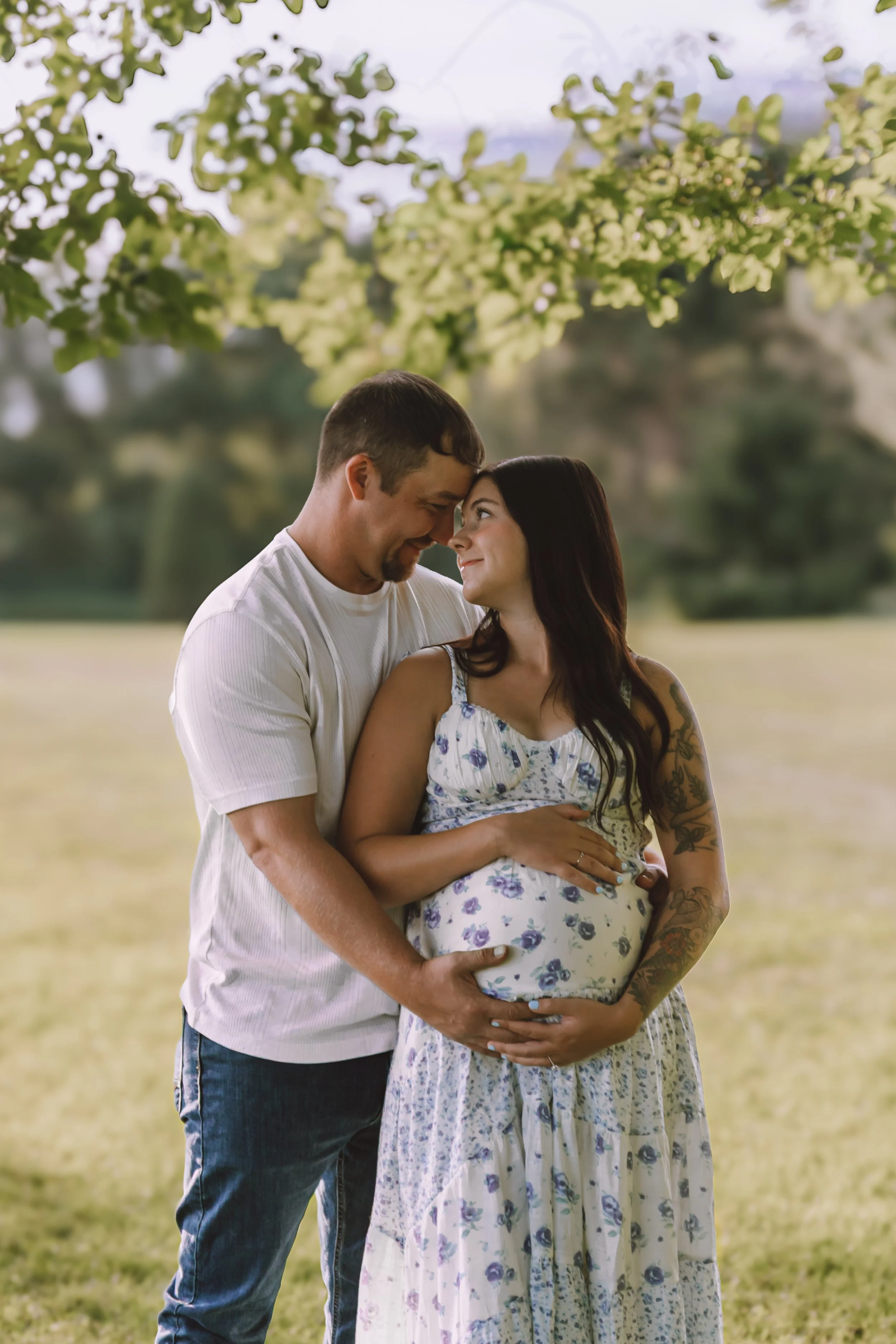 expecting father kissing his partner’s forehead while they hold her belly during an outdoor maternity session near Peoria, Illinois