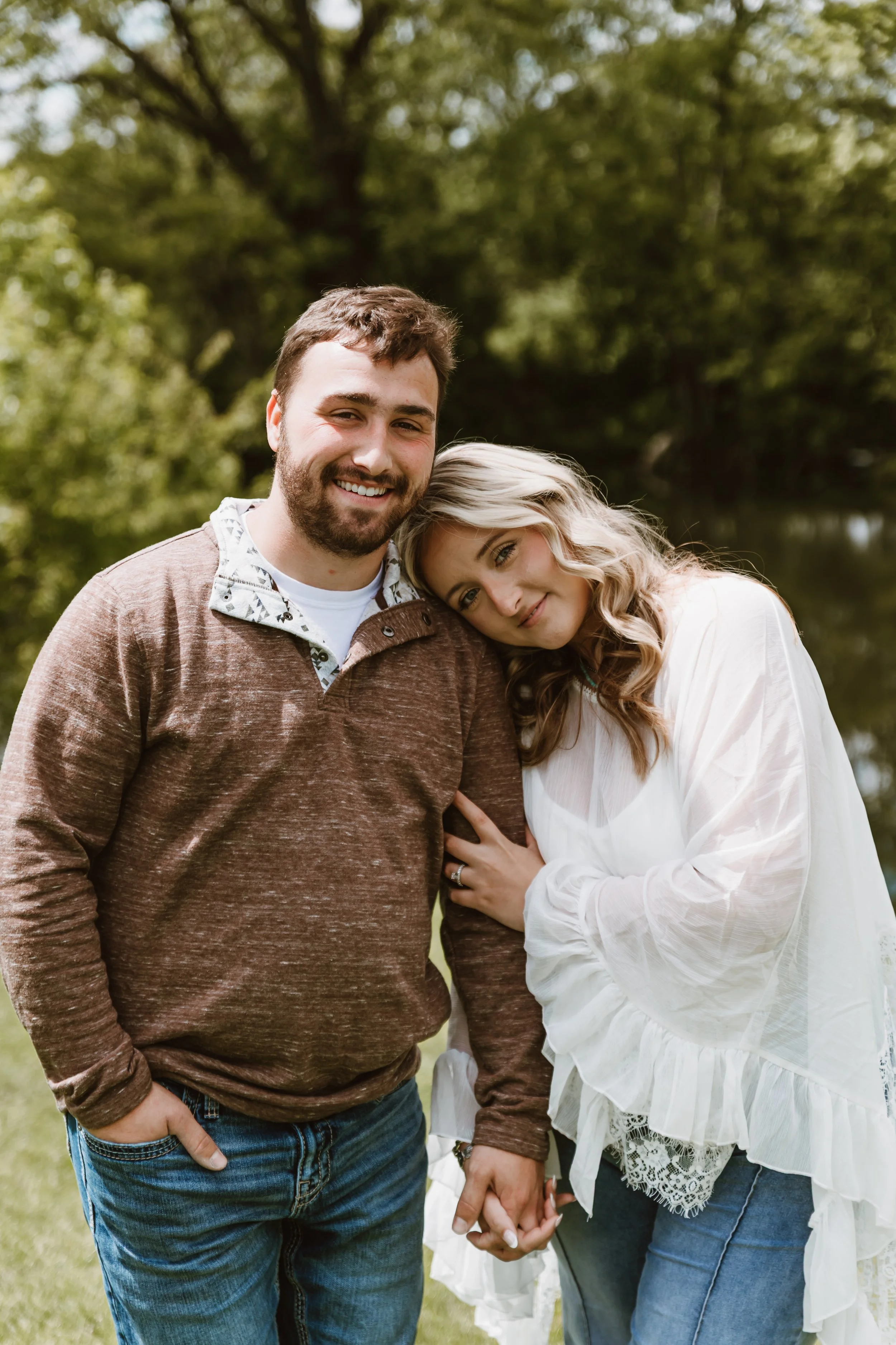 ngaged couple standing under green pine tree branches in central illinois park