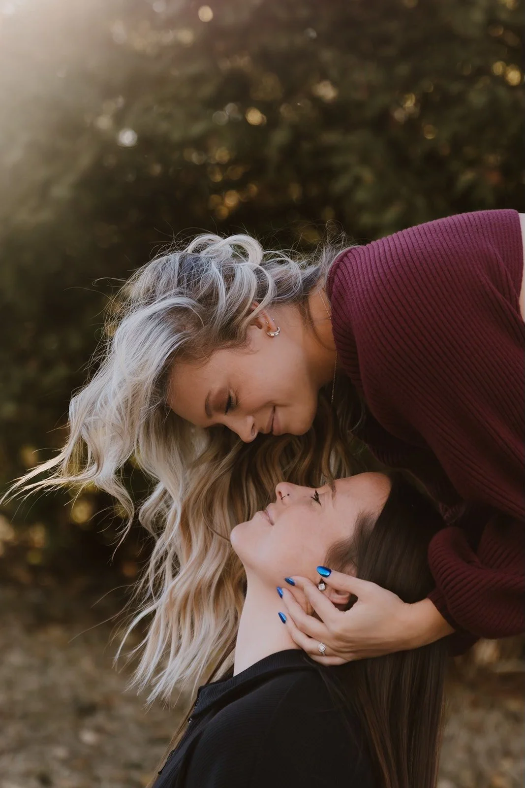 Two women sharing an intimate moment outdoors, leaning close with their foreheads and noses touching, and one woman gently holding the other's face.
