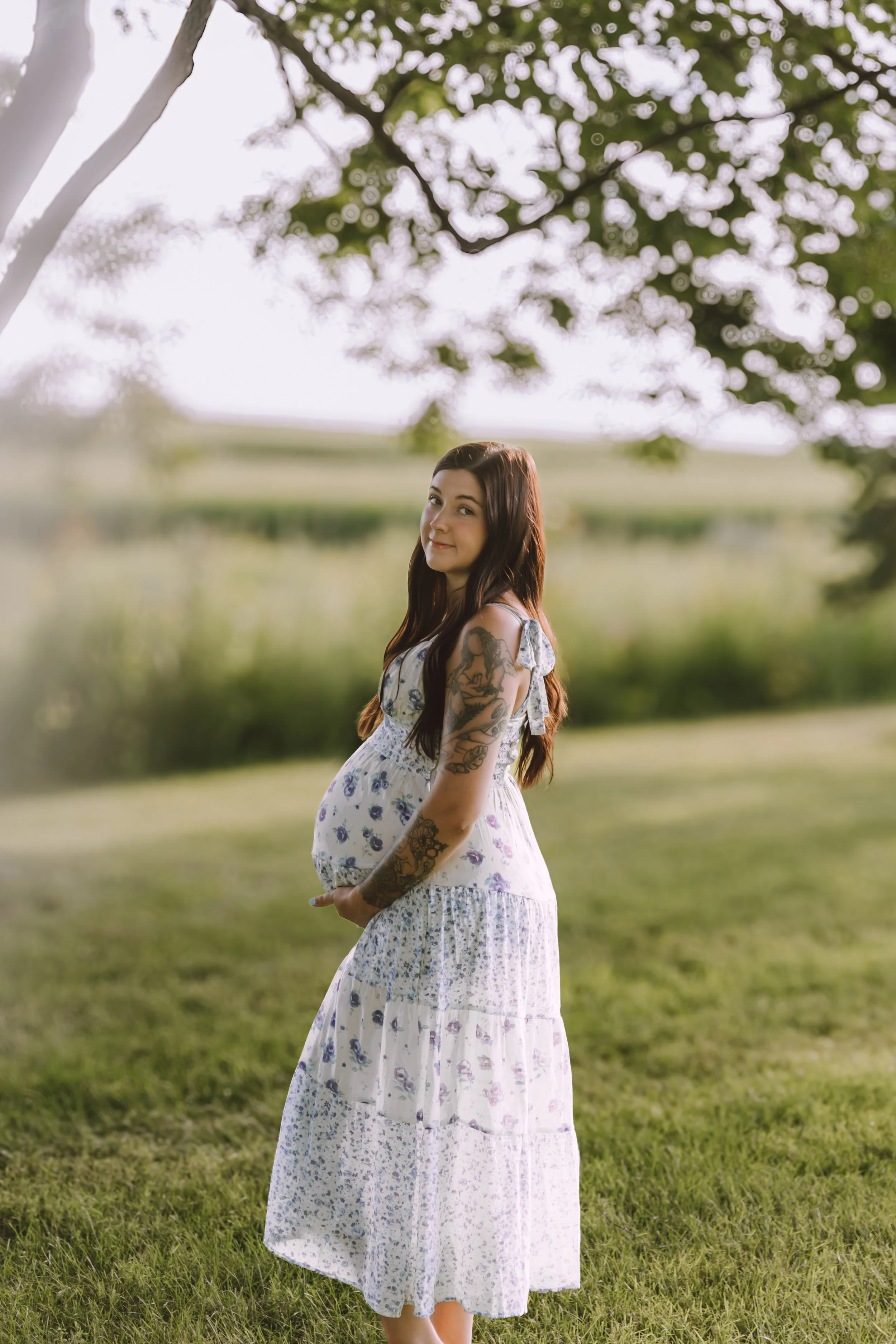 expecting mother wearing a blue floral dress and holding her belly during a summer maternity session in Central Illinois