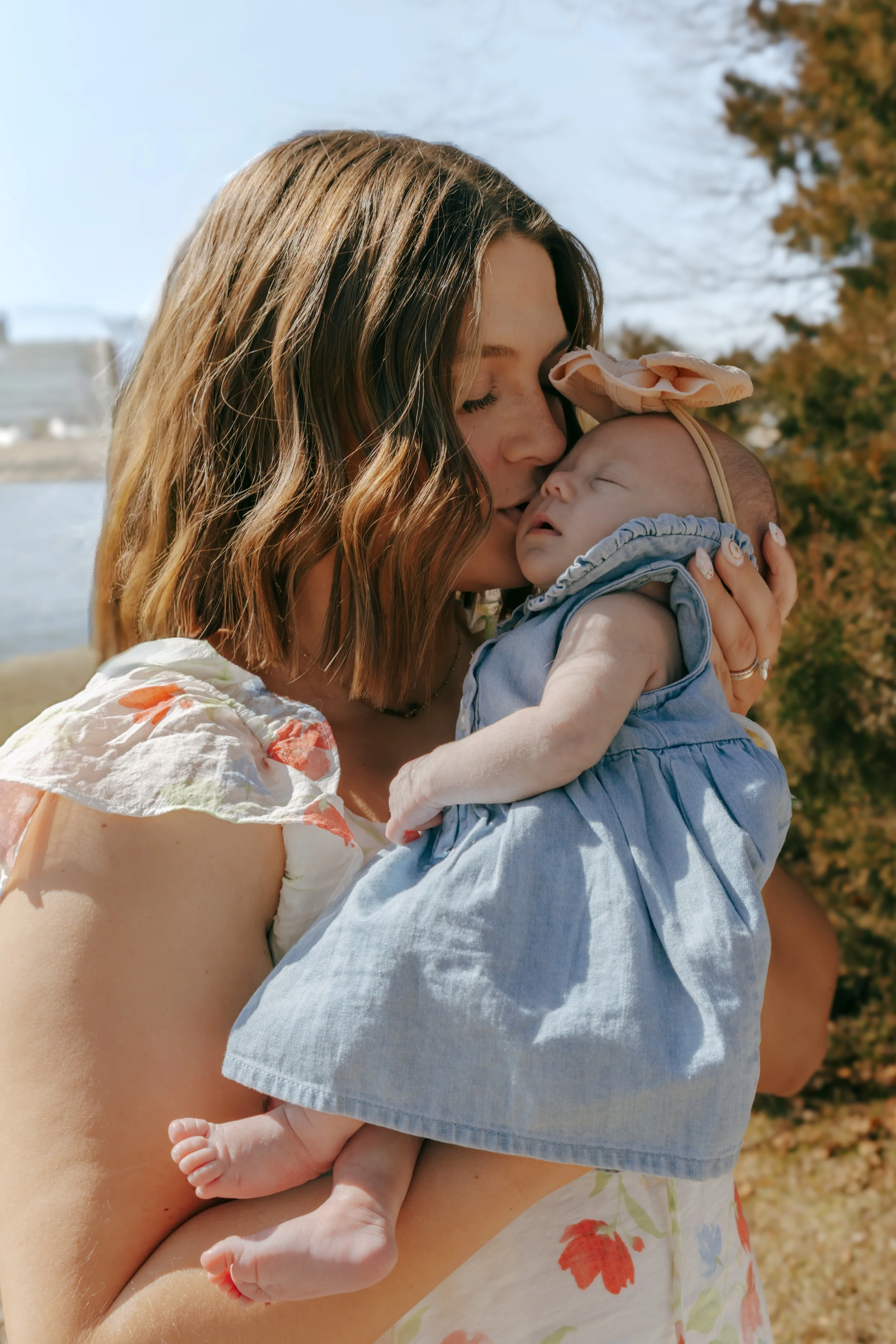 Mother kissing sleeping newborn baby during outdoor family photos at Eureka Lake in Eureka Illinois