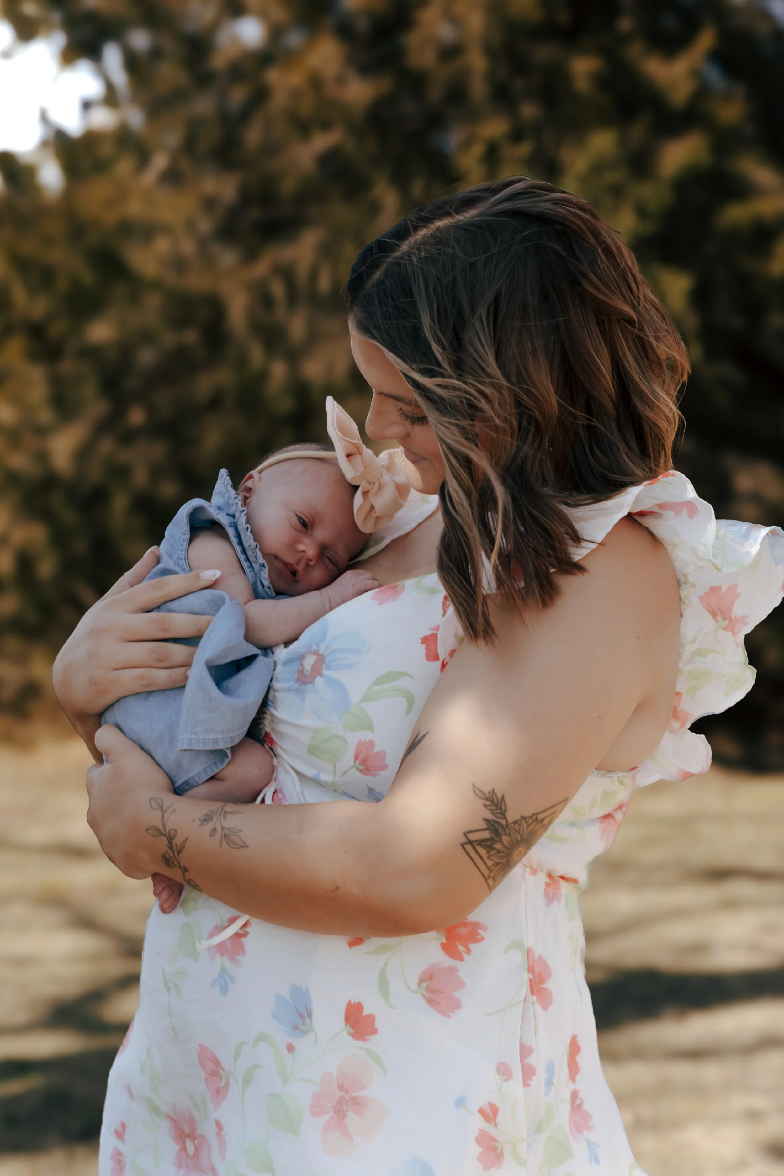 Mom holding sleeping newborn baby in blue dress with bow headband during outdoor family photos at Eureka Lake Illinois