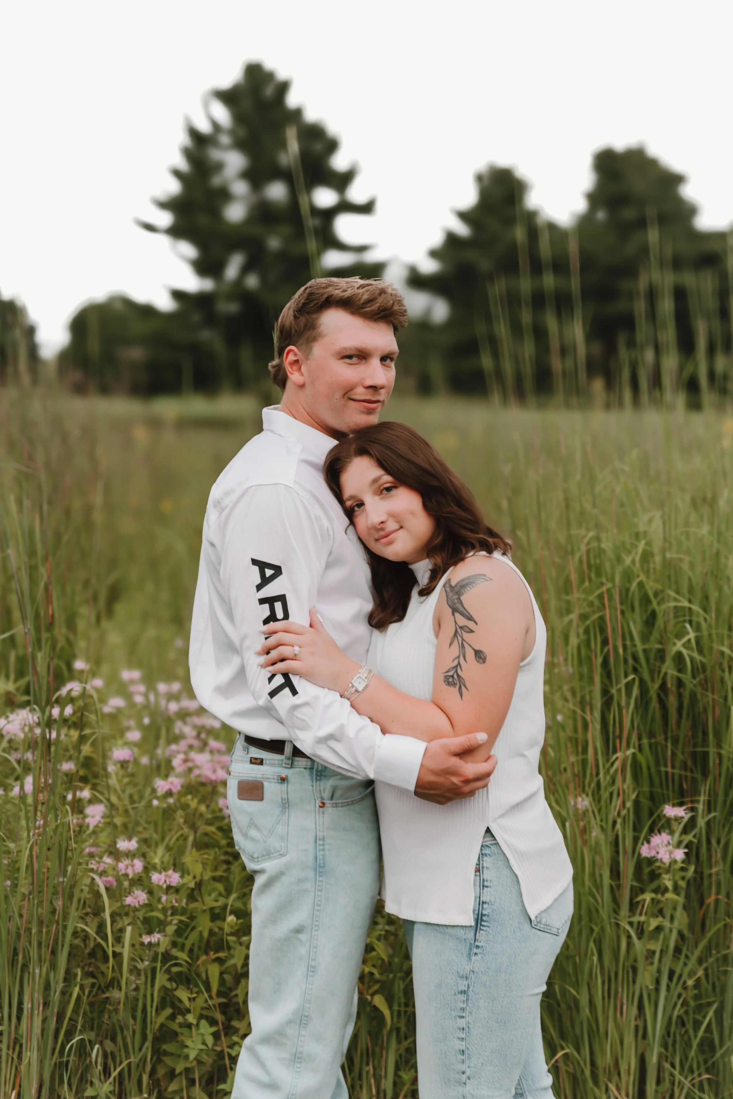 smiling engaged couple in coordinated white and denim outfits posing in a grassy Central Illinois field
