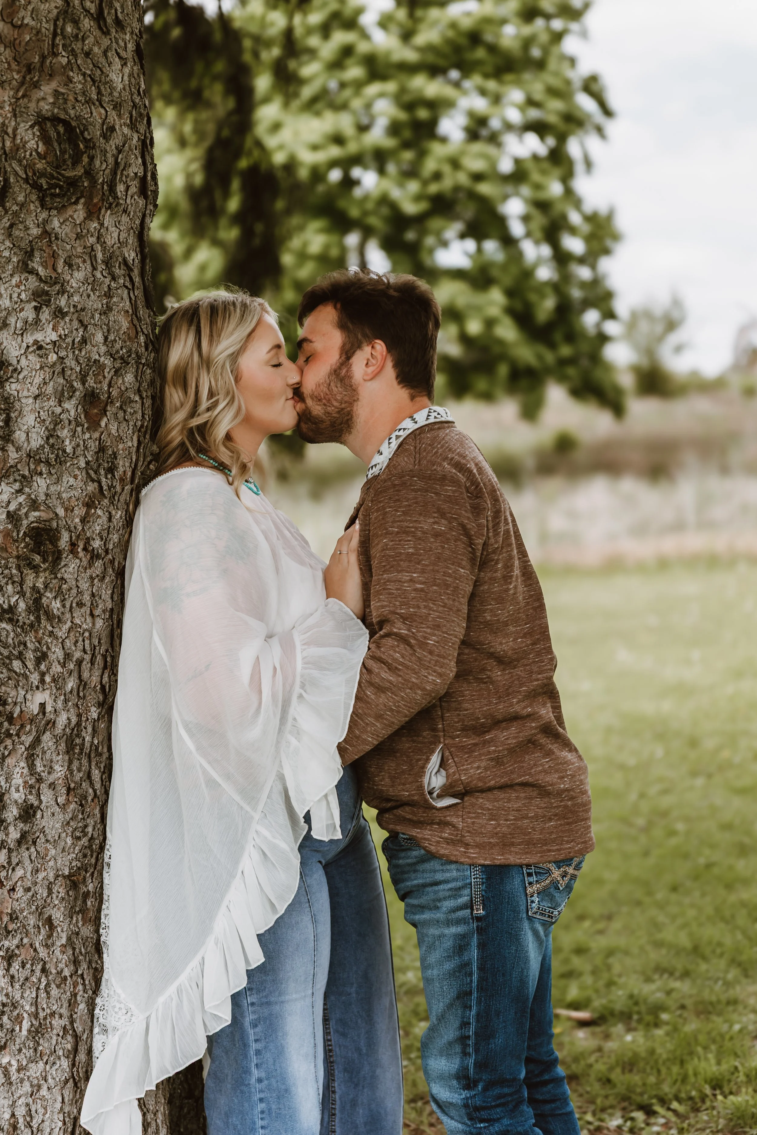 couple kissing and showing engagement ring close up in outdoor setting