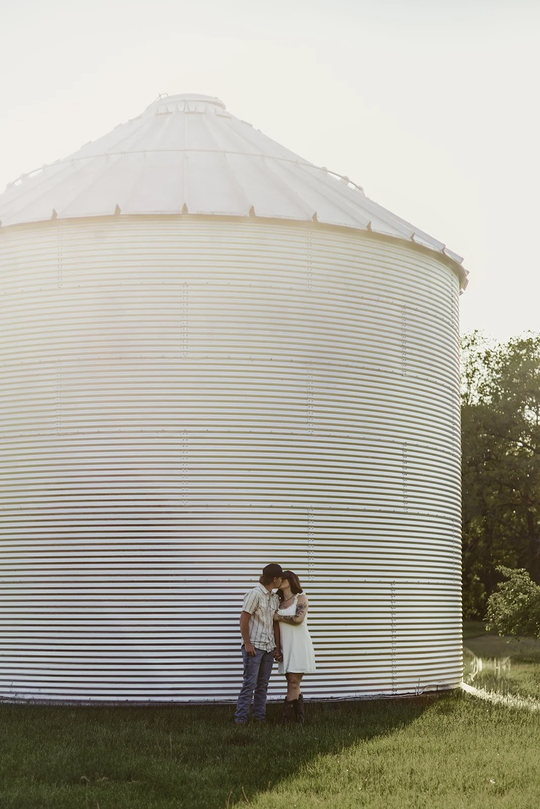 Couple standing beside a large grain bin during golden hour in rural Illinois
