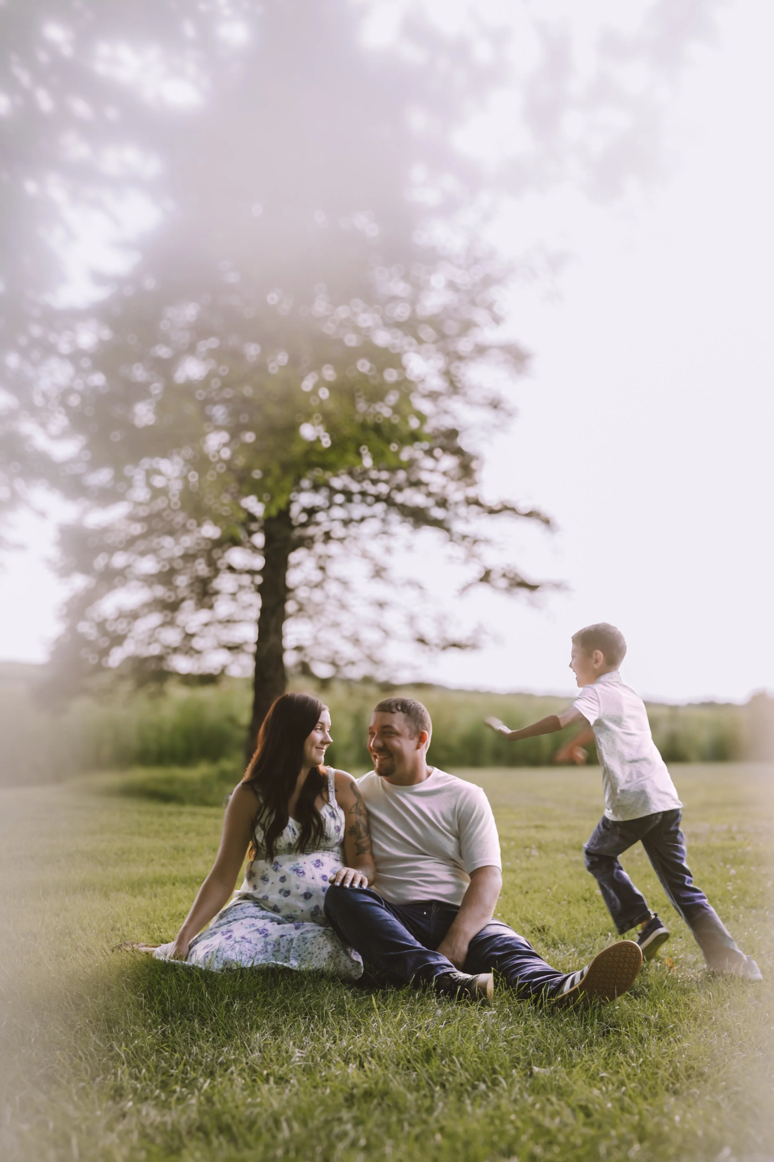 alt text: pregnant mother sitting in the grass while her older son cuddles against her during a summer maternity session in Central Illinois