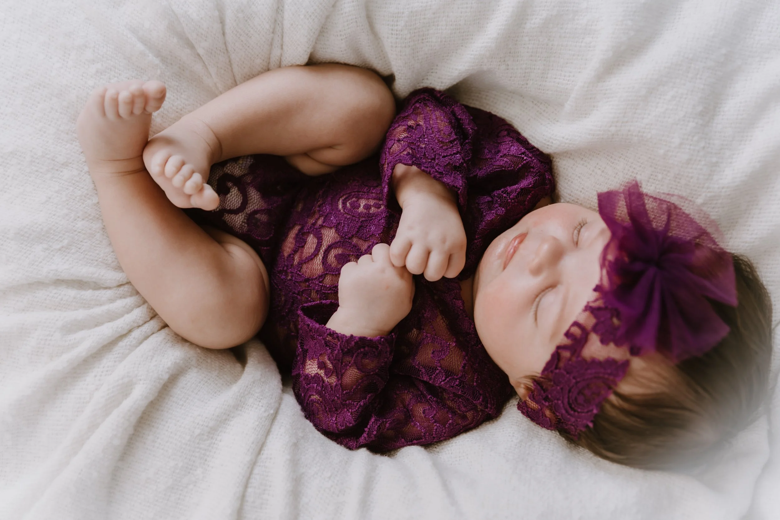 newborn baby girl in purple outfit sleeping curled up