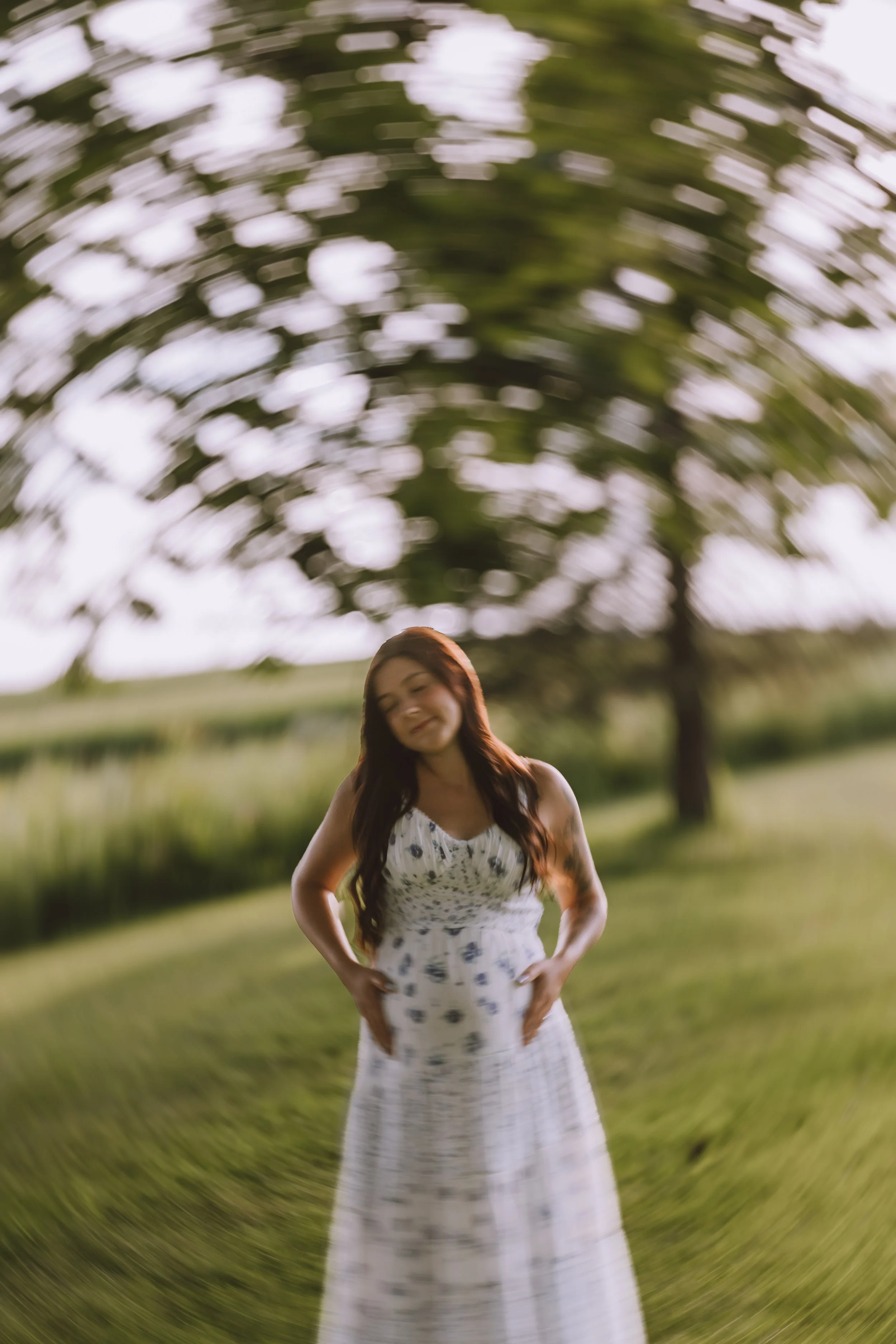 creative motion-blur maternity portrait of a pregnant mother standing beneath a large tree in a blue floral dress