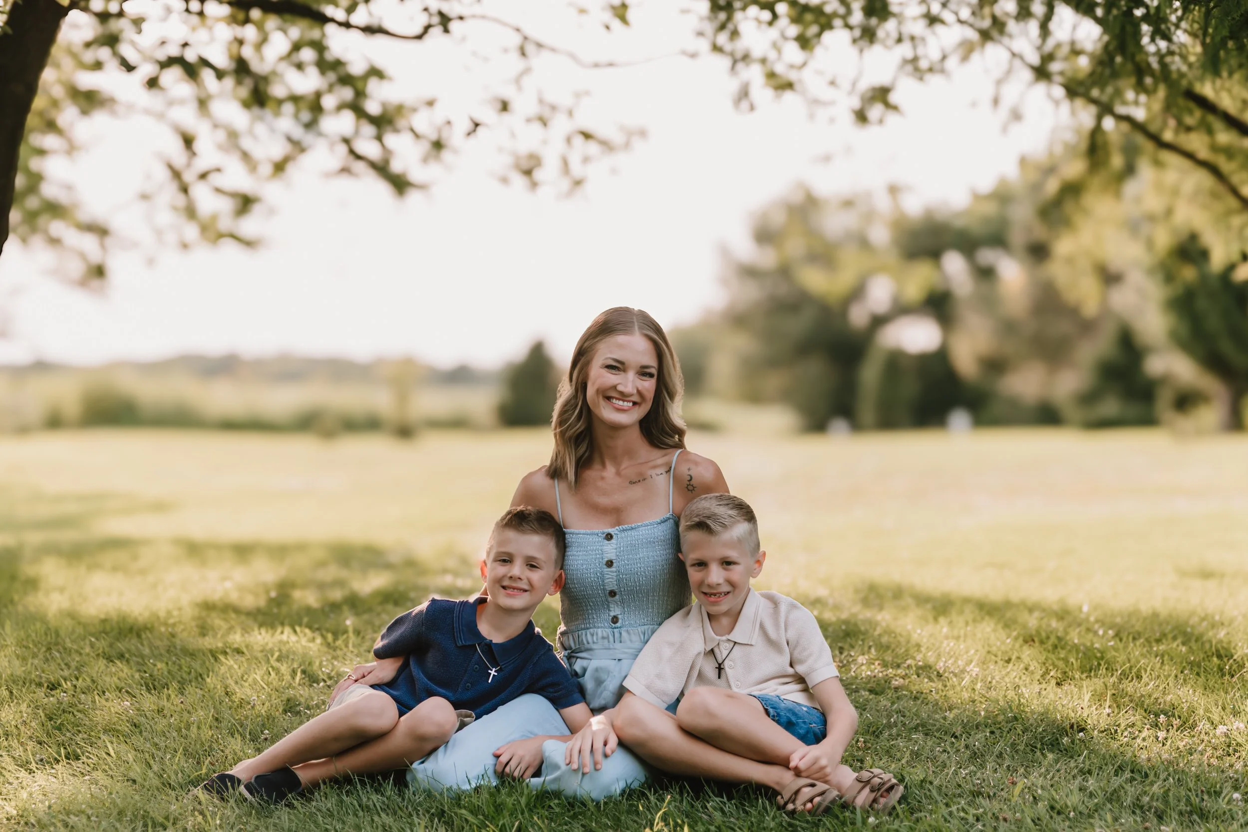 Mother sitting in the grass with her two sons during an outdoor family photography session near Peoria, Illinois.