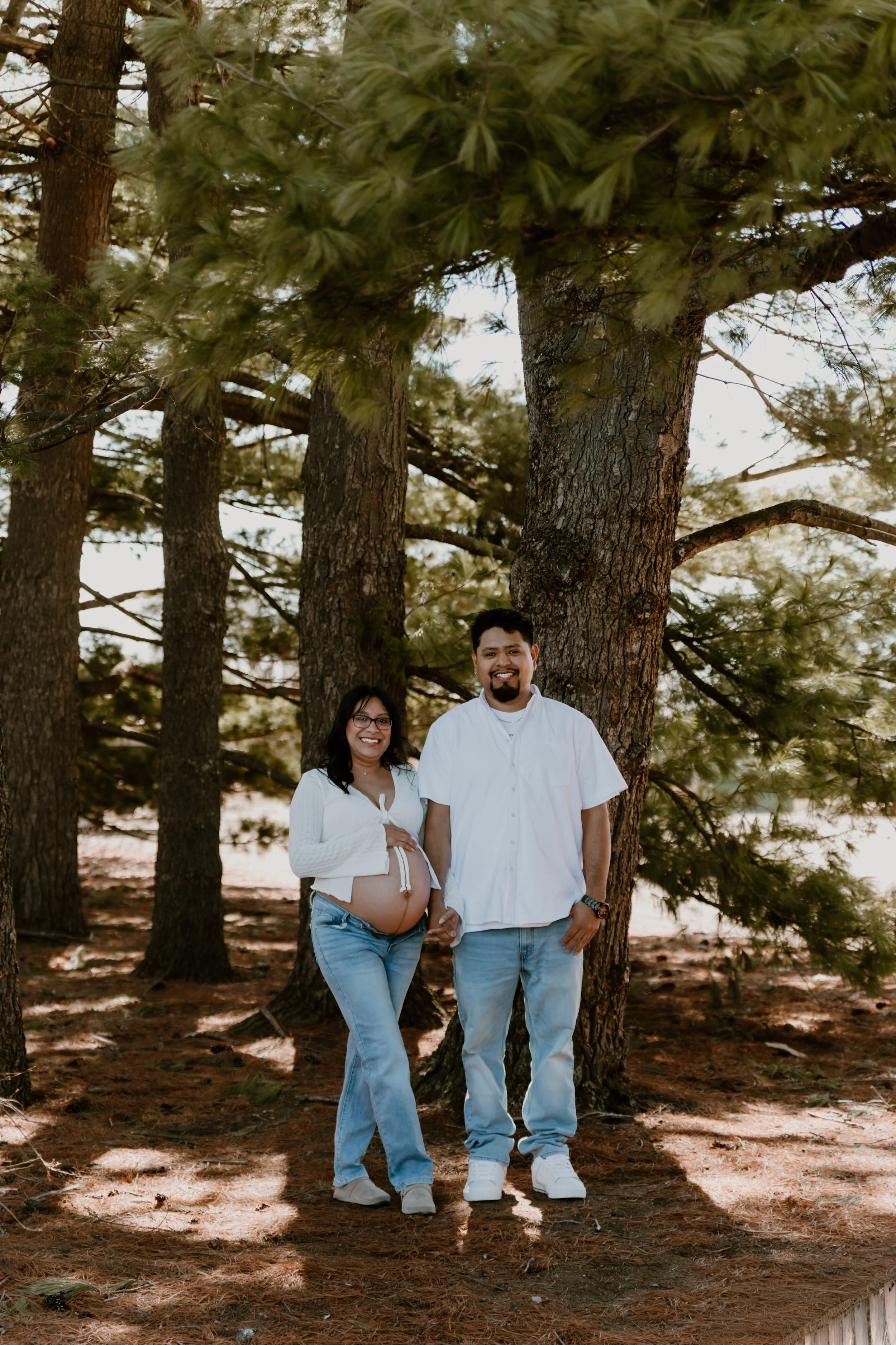 pregnant couple standing under pine trees maternity photos
