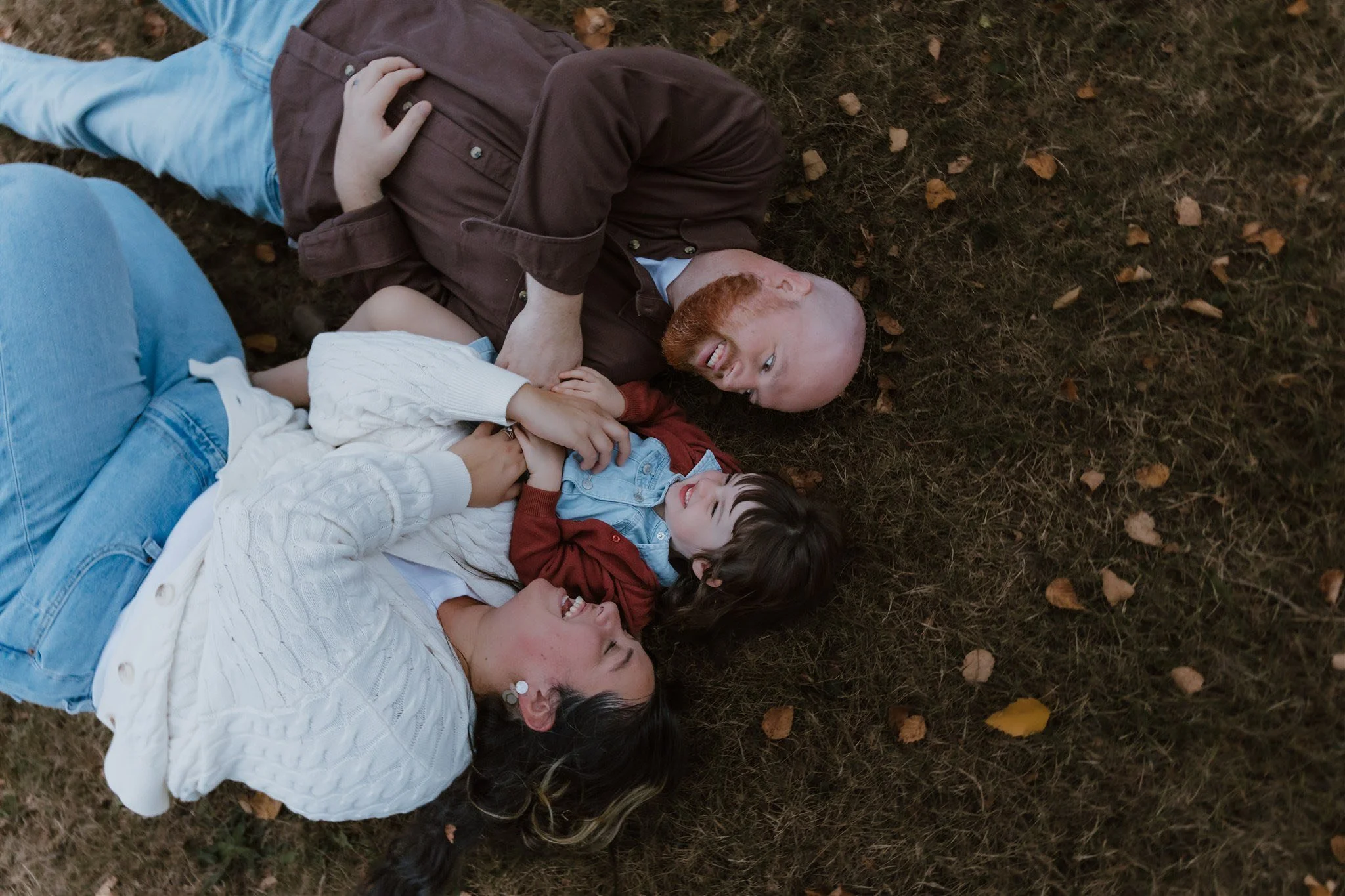 A family of three lying on the grass, smiling and laughing together.