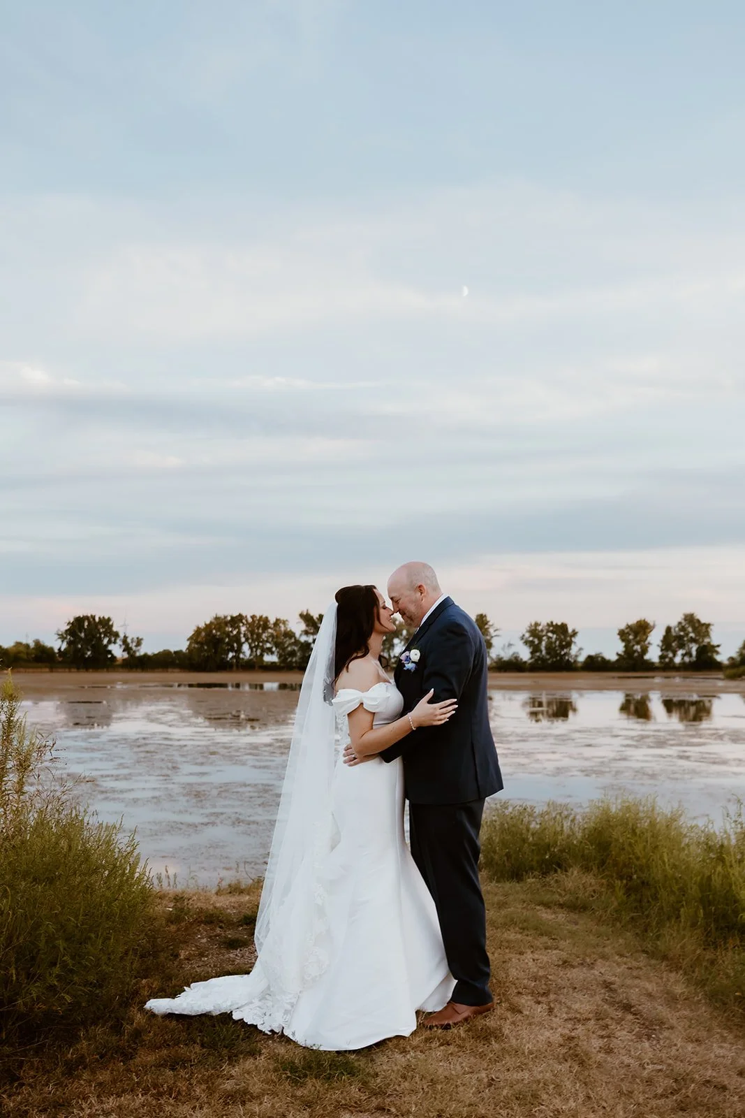 bride and groom hugging in front of lake