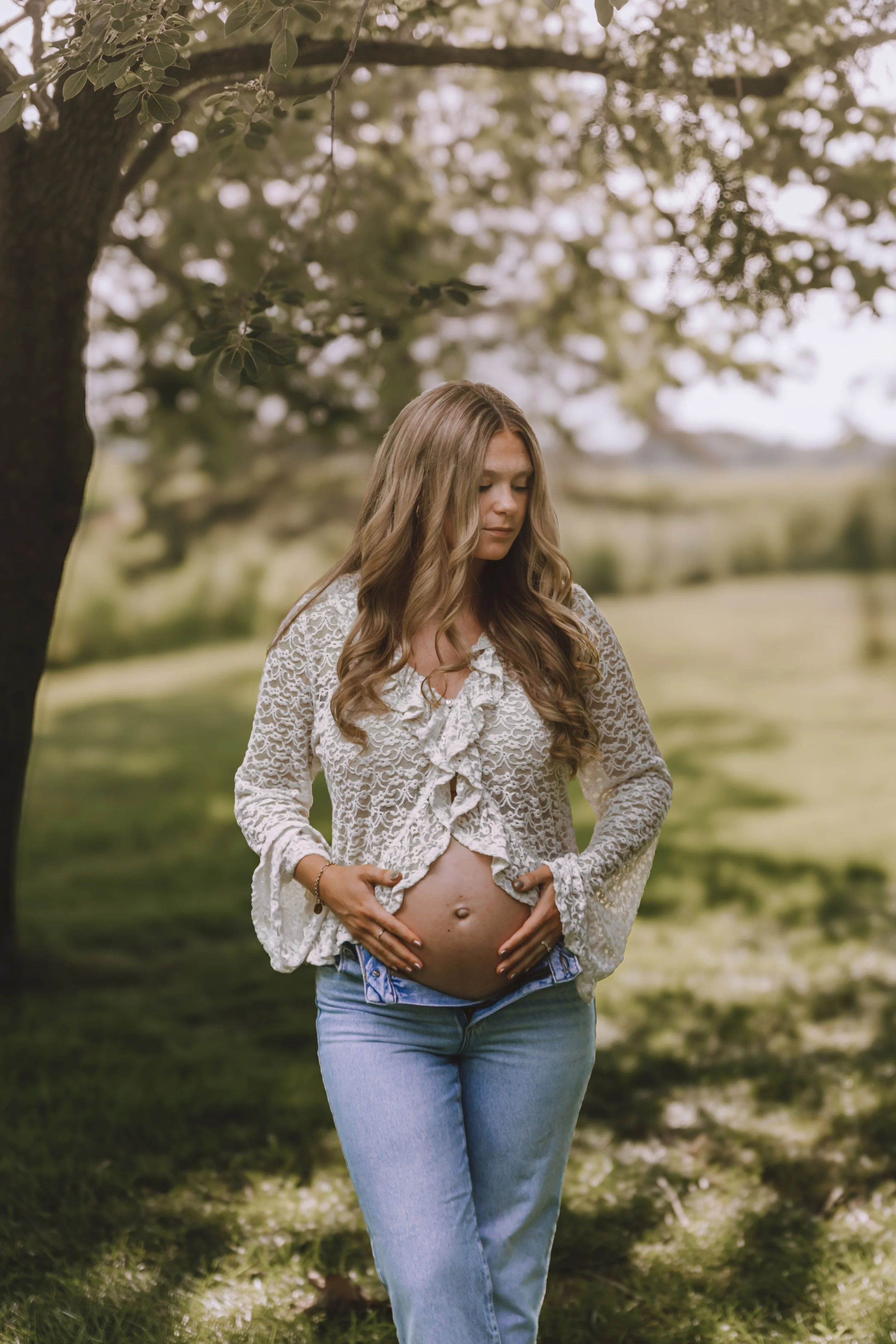 Expecting mother standing beneath trees during a relaxed outdoor maternity photography session in Central Illinois.