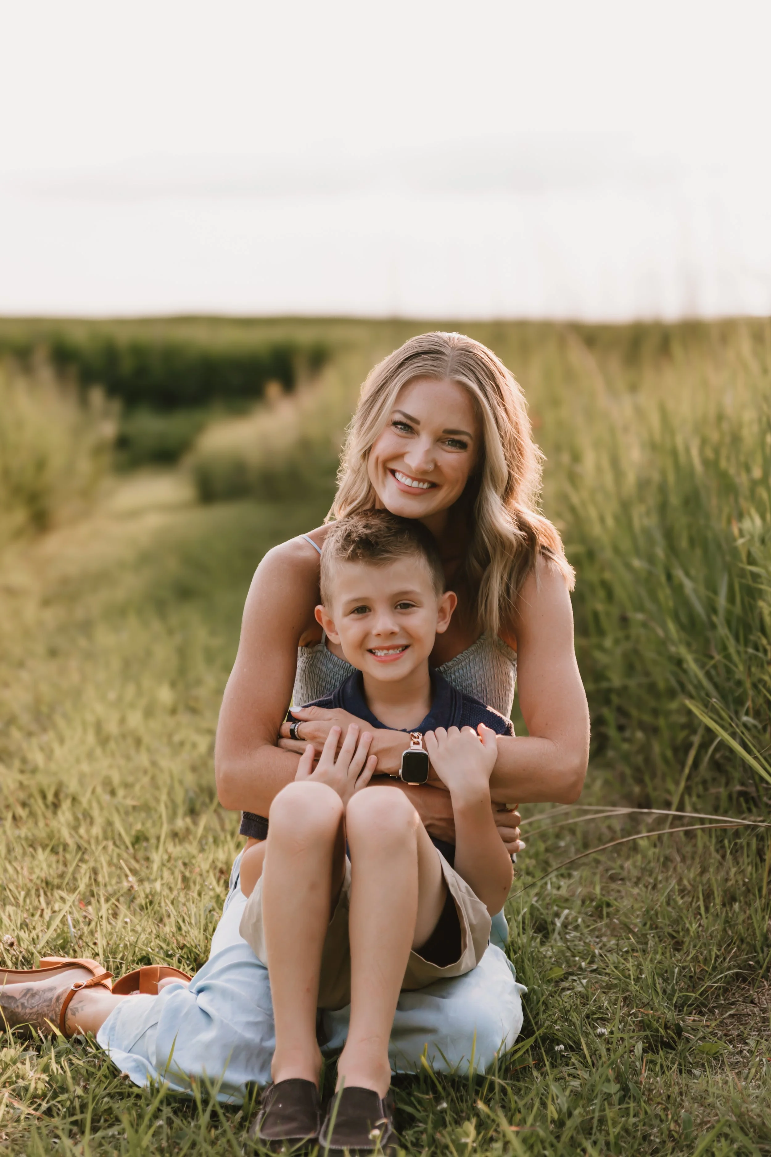 Mother hugging her oldest son while sitting in a grassy field during golden hour family portraits in Central Illinois.