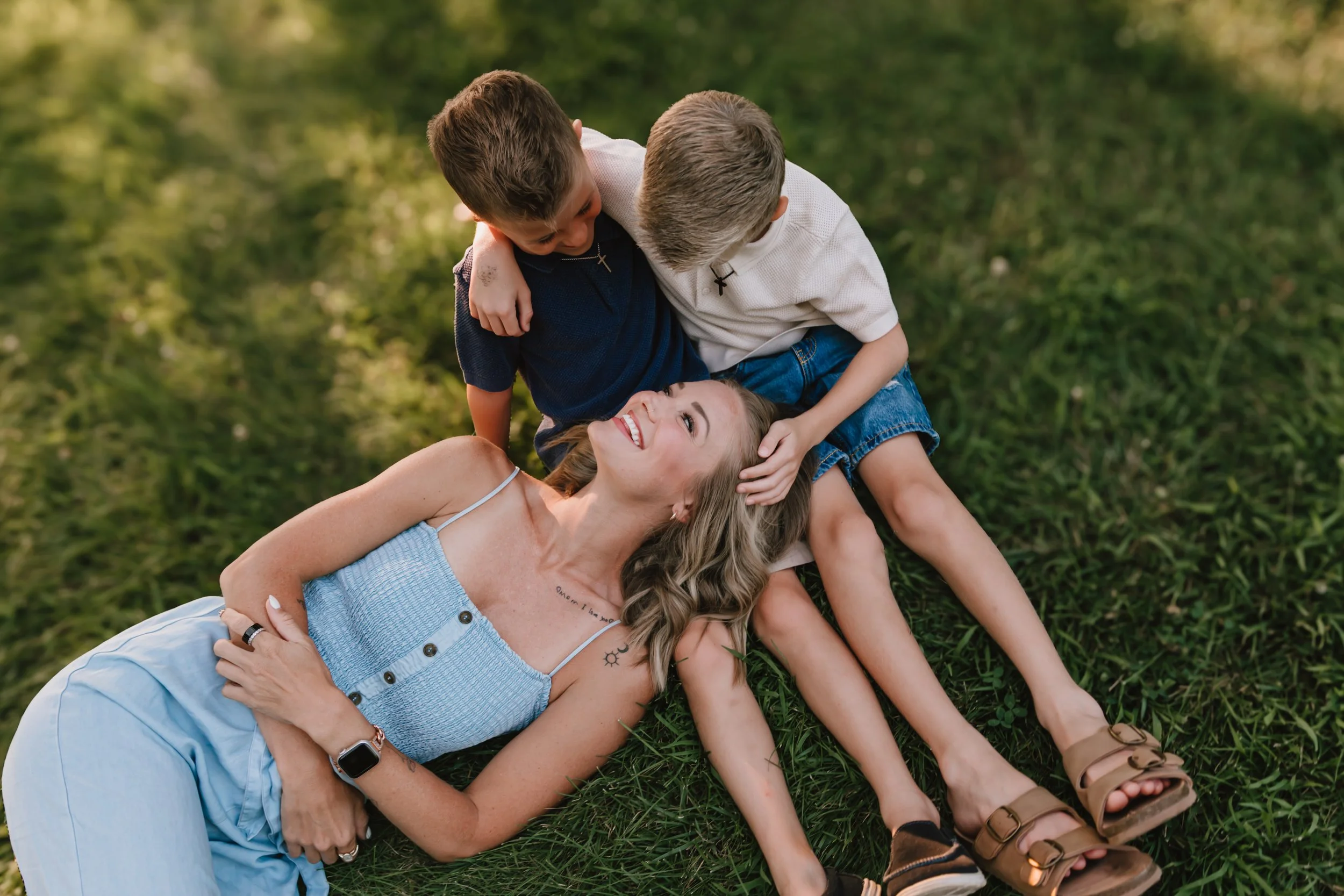 Two young brothers hugging their mom while she laughs during a relaxed outdoor family session in Central Illinois.