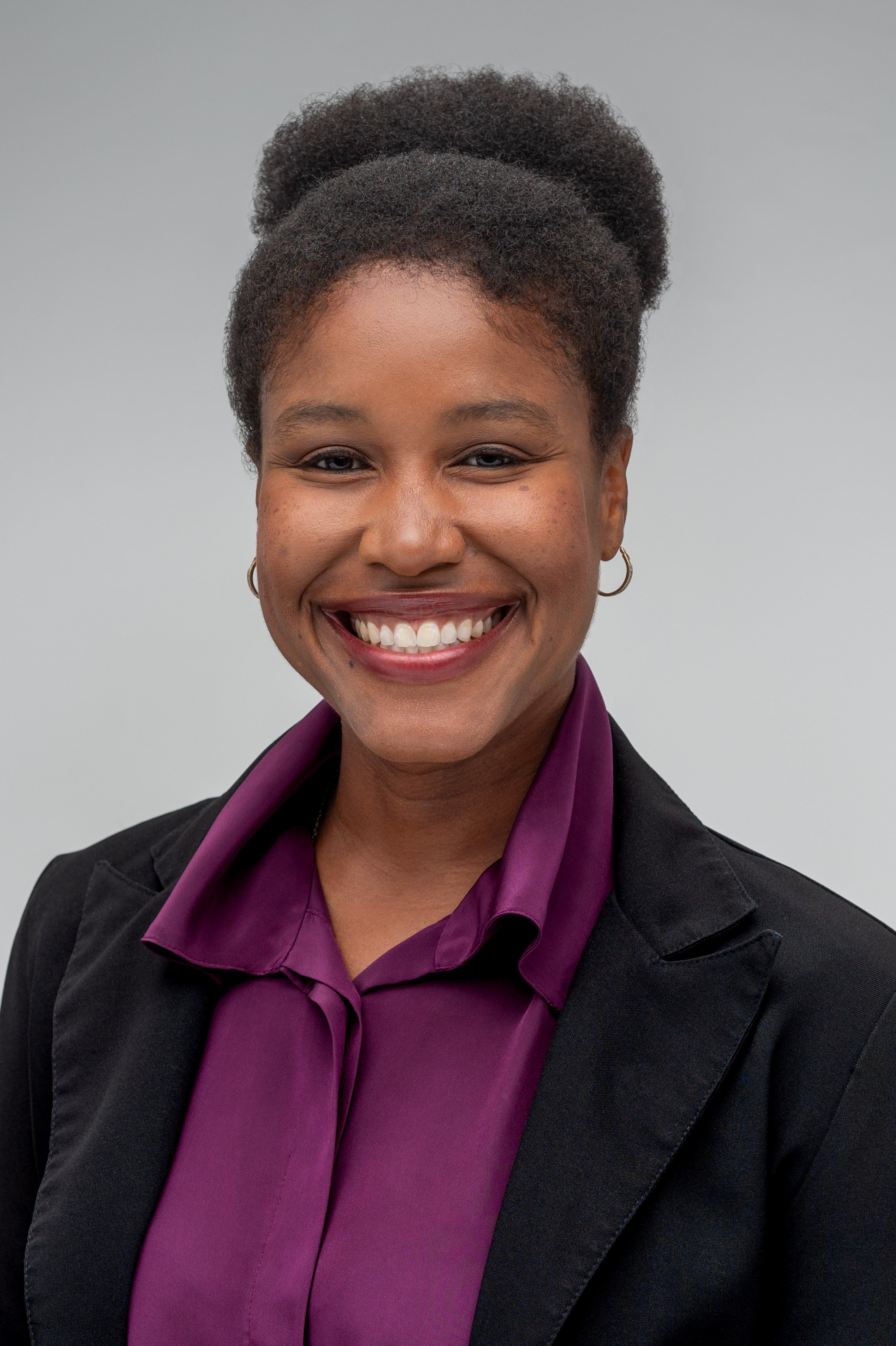 Whitney Parnell, a Black woman, smiling in a professional headshot with her hair styled in an updo, wearing a black blazer and purple blouse against a light gray background.