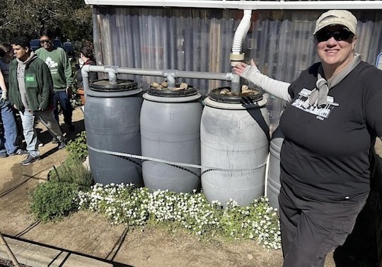 Water-saving workshop instructor Kat Sawyer standing in front of a trio of rain barrels.
