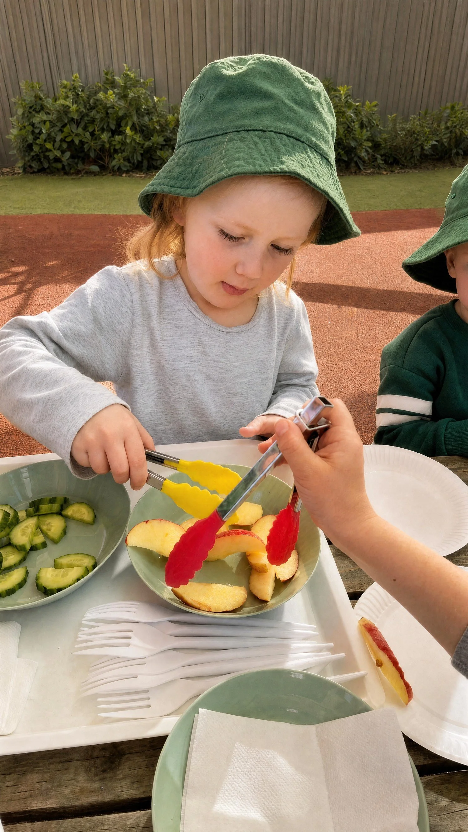 Child serving fruit with tongs at mealtime