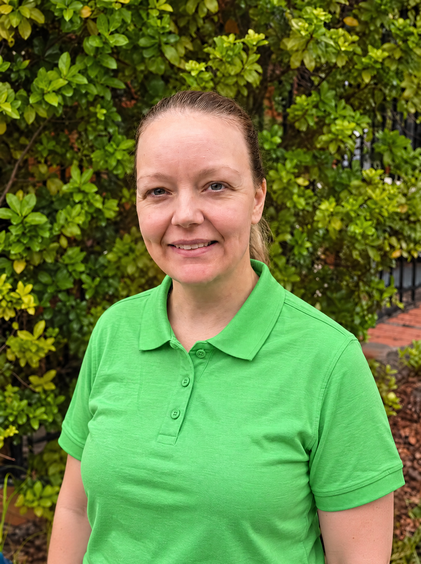 Woman smiling in front of a brick wall wearing a lime green polo shirt with black long sleeves underneath.