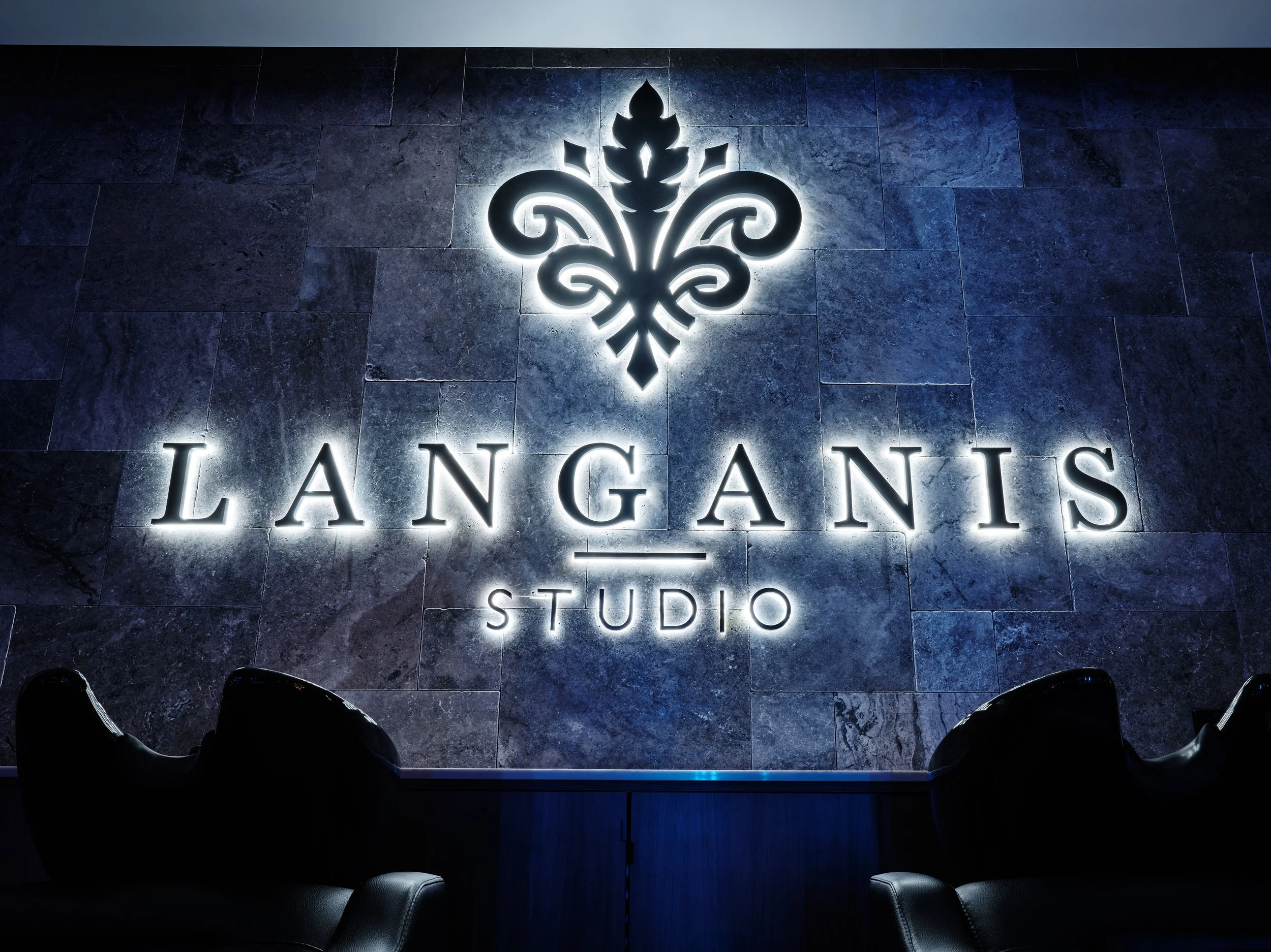 Backlit sign on a dark stone wall that reads 'Langanis Studio' with an ornate emblem above.