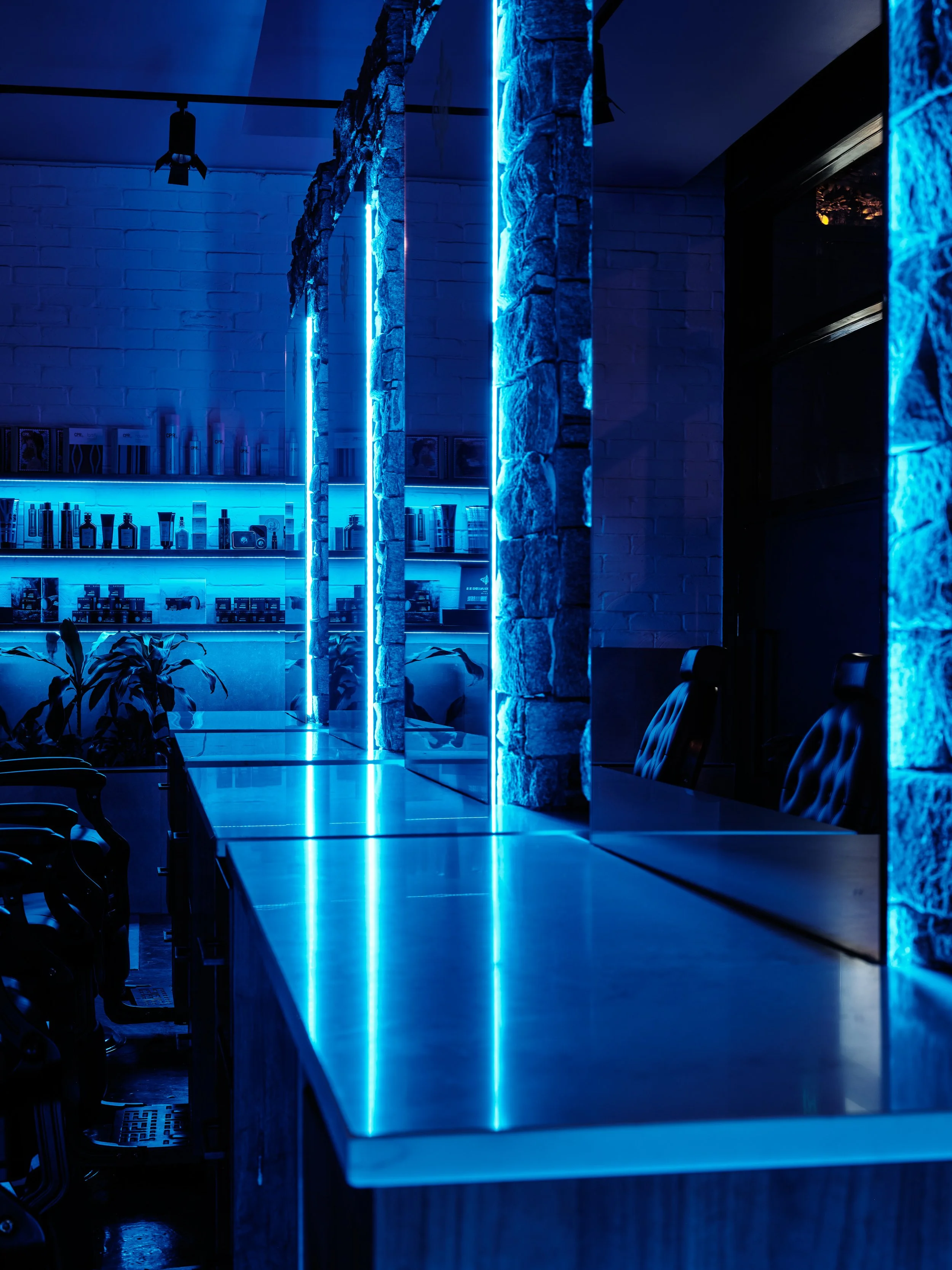 A modern interior with blue neon lighting, stone pillars, black chairs, and shelves with various bottles and products.