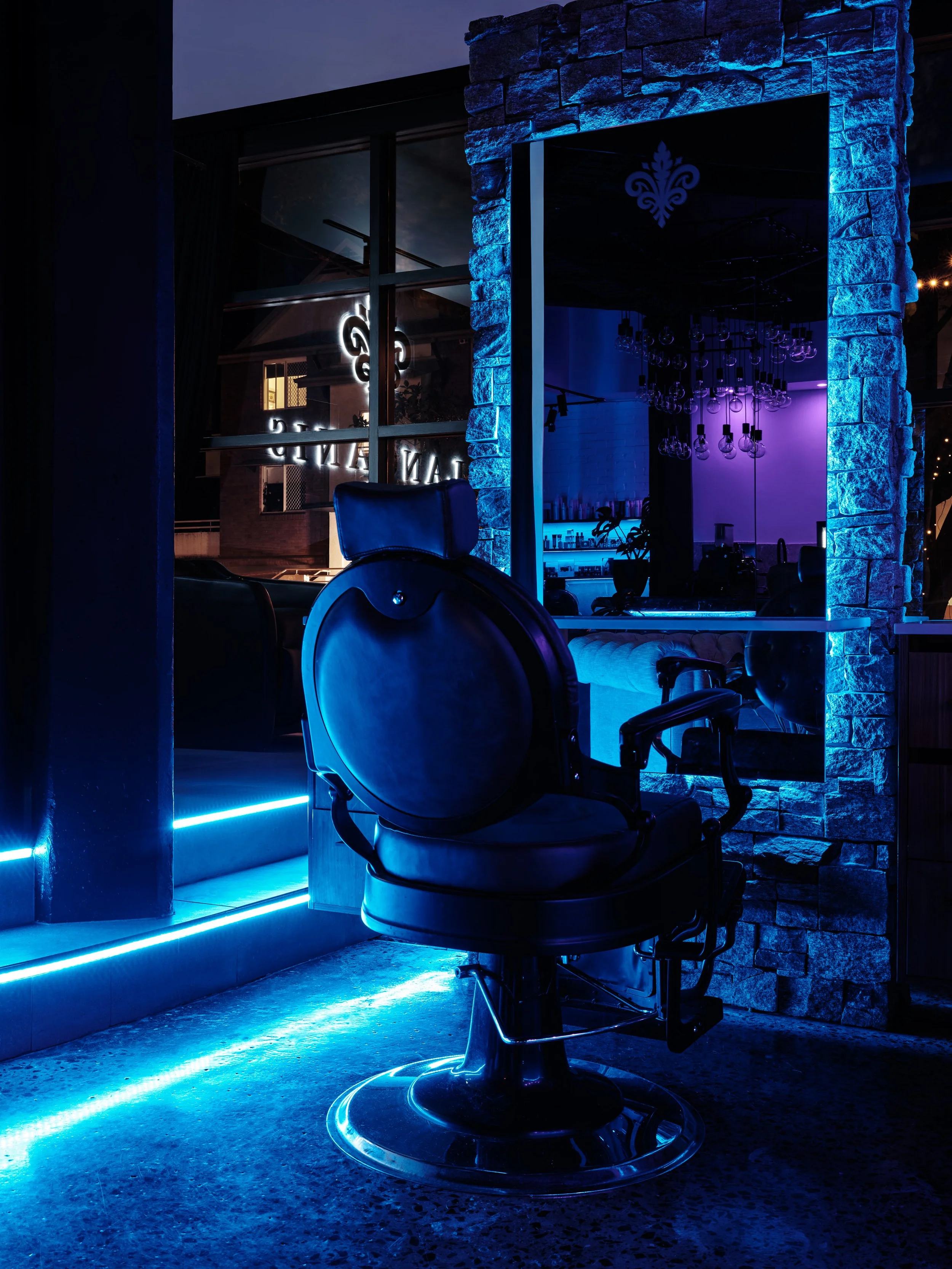 Barbershop chair with blue neon lighting, inside a modern salon with brick walls and large window reflecting interior lights.