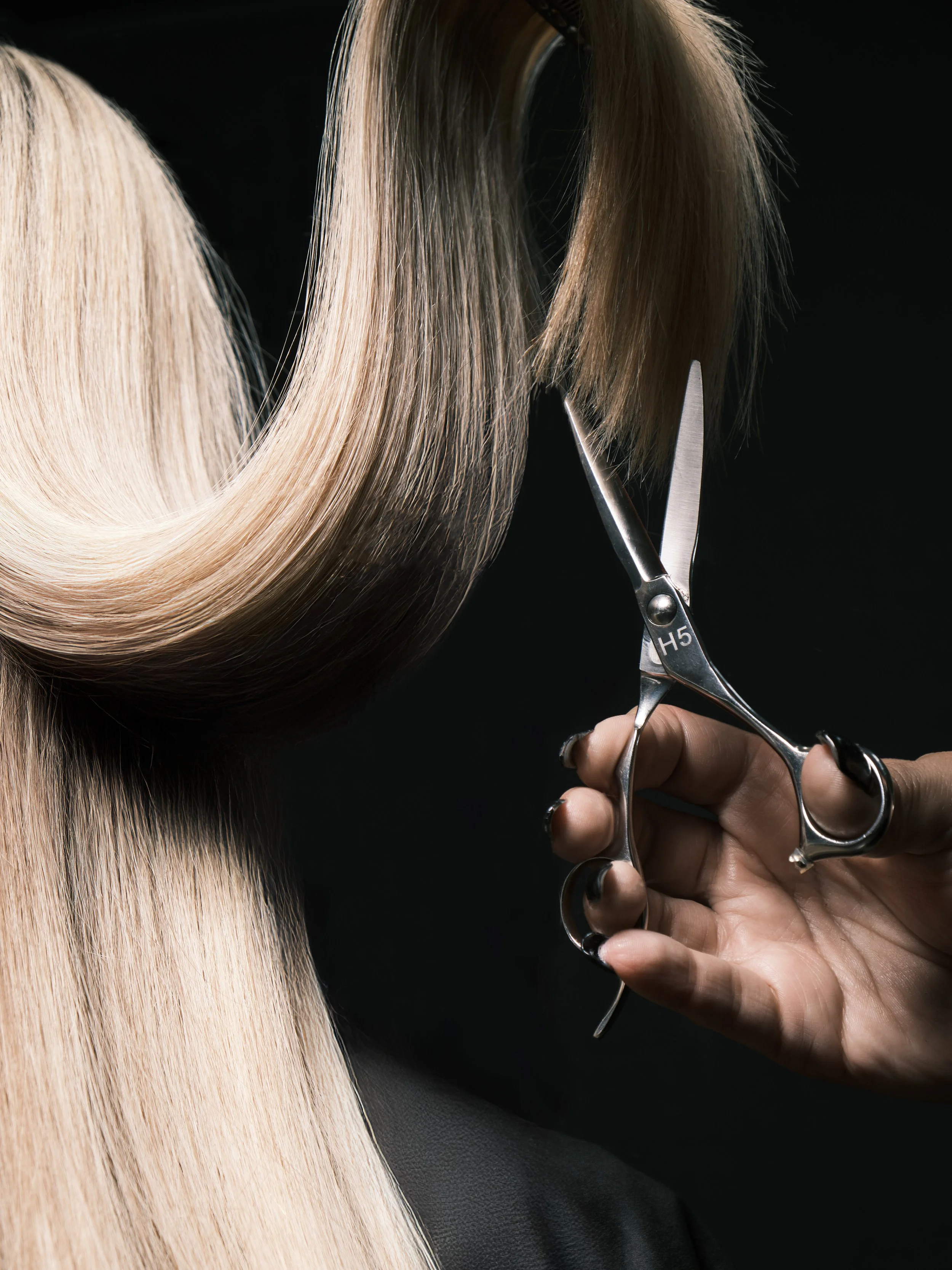 Close-up of a hairstylist cutting long, blonde hair with scissors.