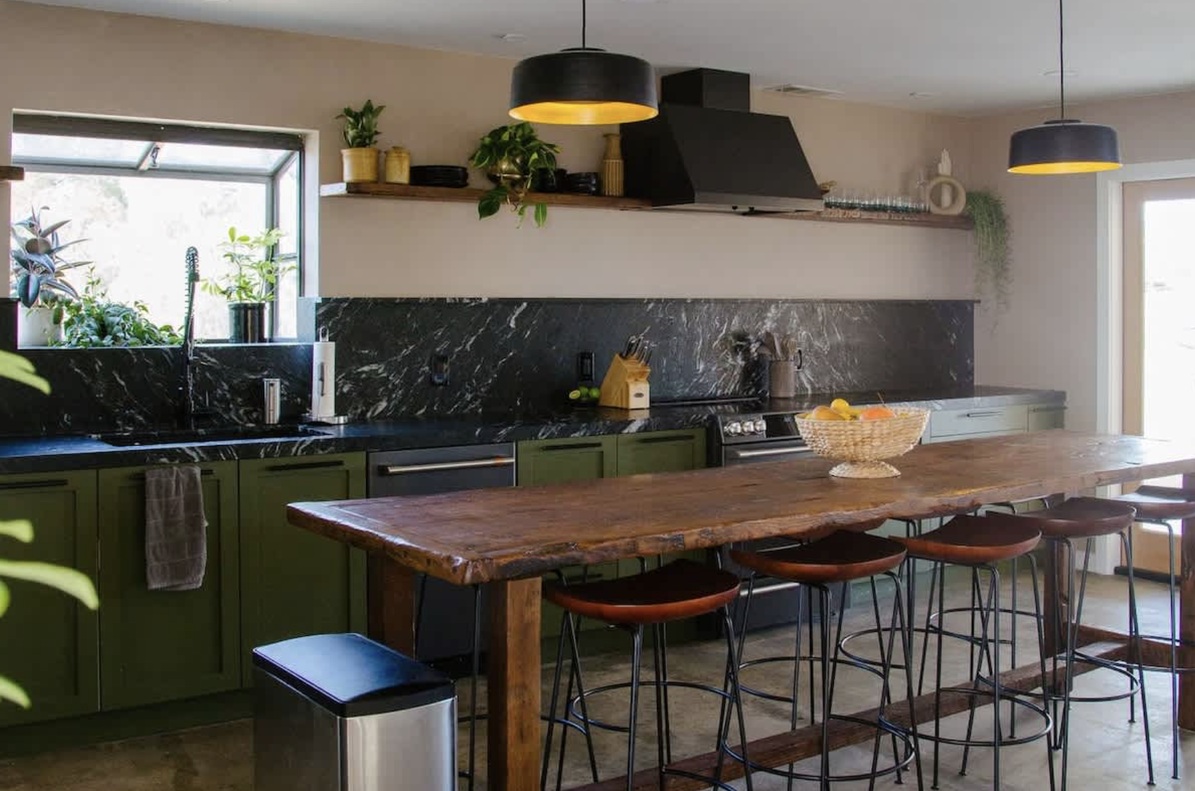 Modern kitchen with green cabinets, black marble countertops, and a large wooden island with four bar stools.