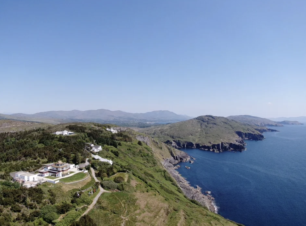 Coastal landscape in south Ireland featuring green hills, scattered white houses, and rocky cliffs along the ocean under a clear blue sky.
