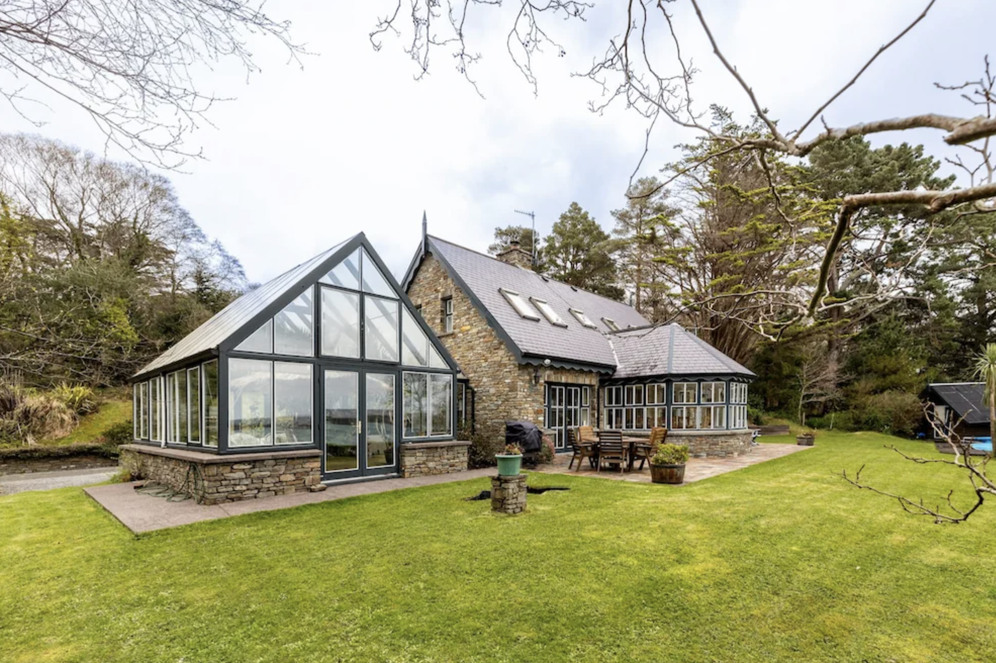 a traditional stone house in Ireland with a modern glass extension, surrounded by a well-maintained lawn and trees.