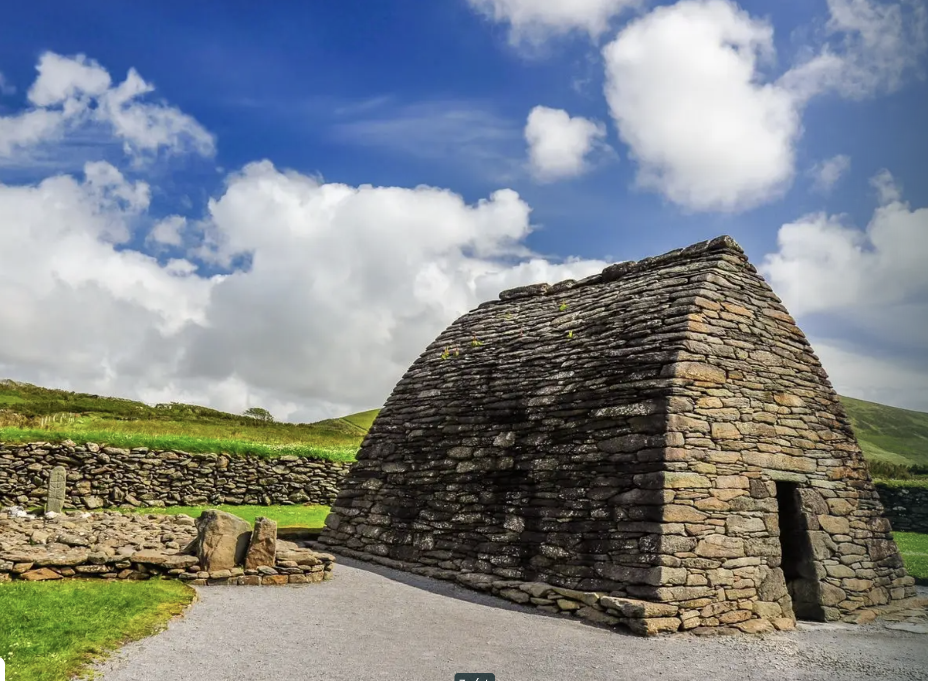 An ancient stone structure built with layered stones, set in a green landscape under a partly cloudy sky.