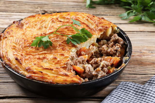 A shepherd's pie with a golden mashed potato crust and ground meat filling, garnished with parsley, on a rustic wooden table.