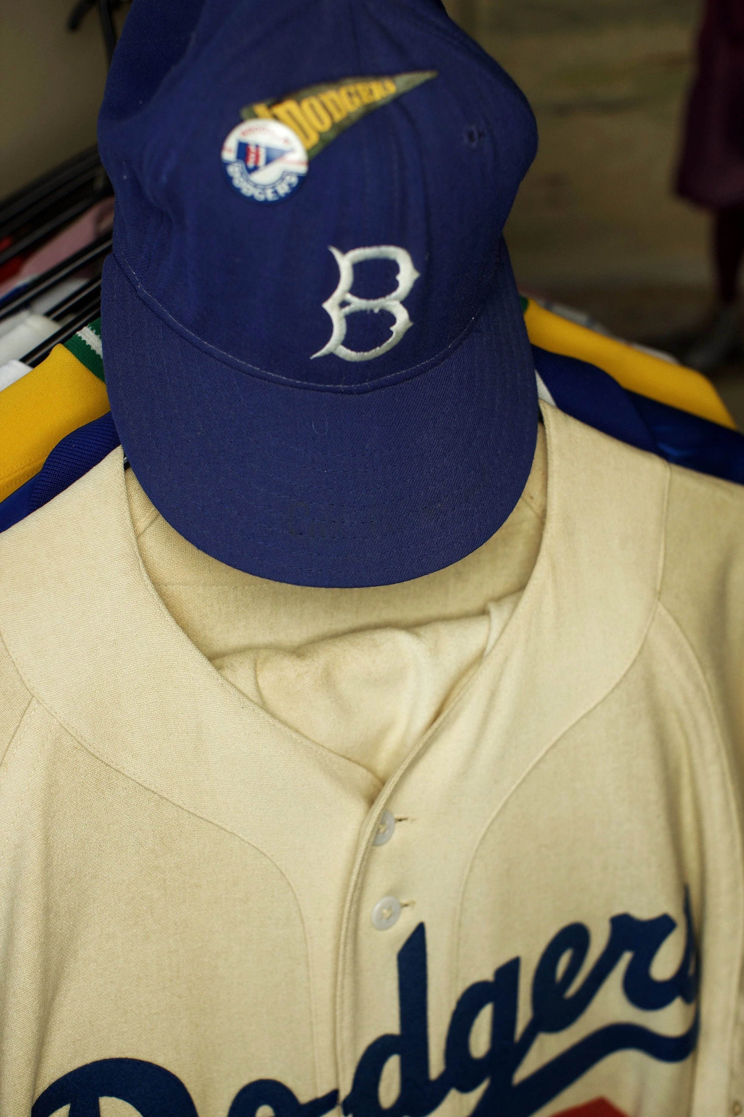 A blue baseball cap with the letter B embroidered on the front, worn over a beige jacket with dark blue text.
