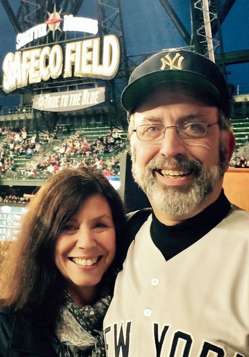 Smiling man and woman taking a selfie at Yankee Stadium with the Sign 'SAFECO FIELD' in the background.