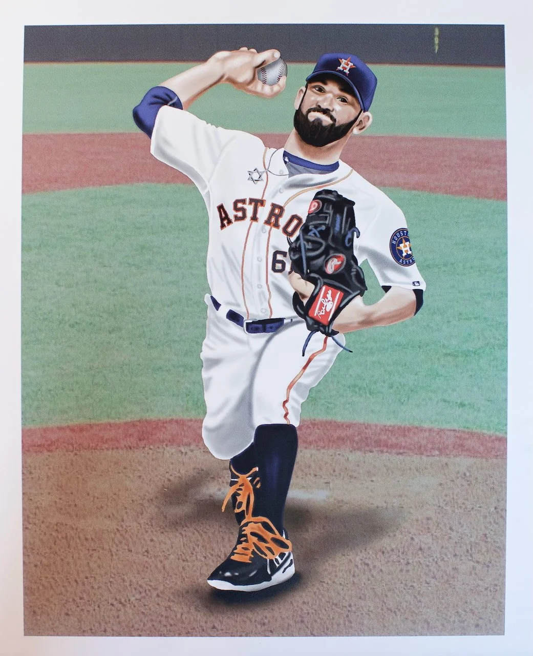 A baseball player in an Houston Astros uniform stands on the pitcher's mound, holding a baseball in his right hand, and wearing a black glove on his left hand. He is smiling and sitting on one leg with orange and black shoes.