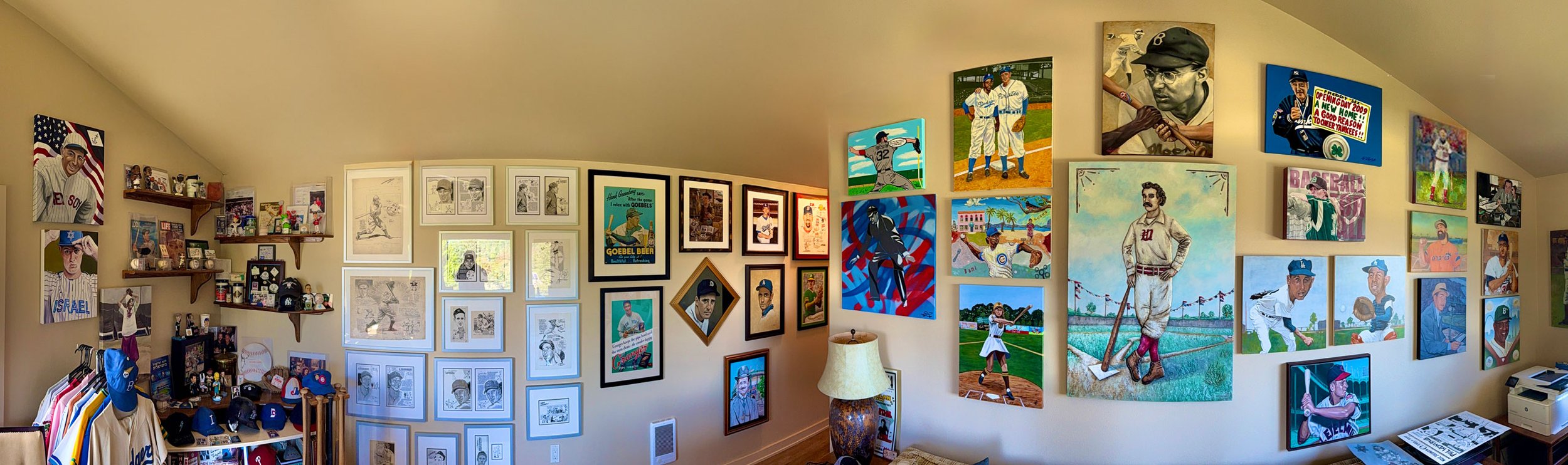 A room decorated with numerous framed pictures and artwork of baseball players, including posters, illustrations, and photographs, with shelves displaying memorabilia and clothing items.
