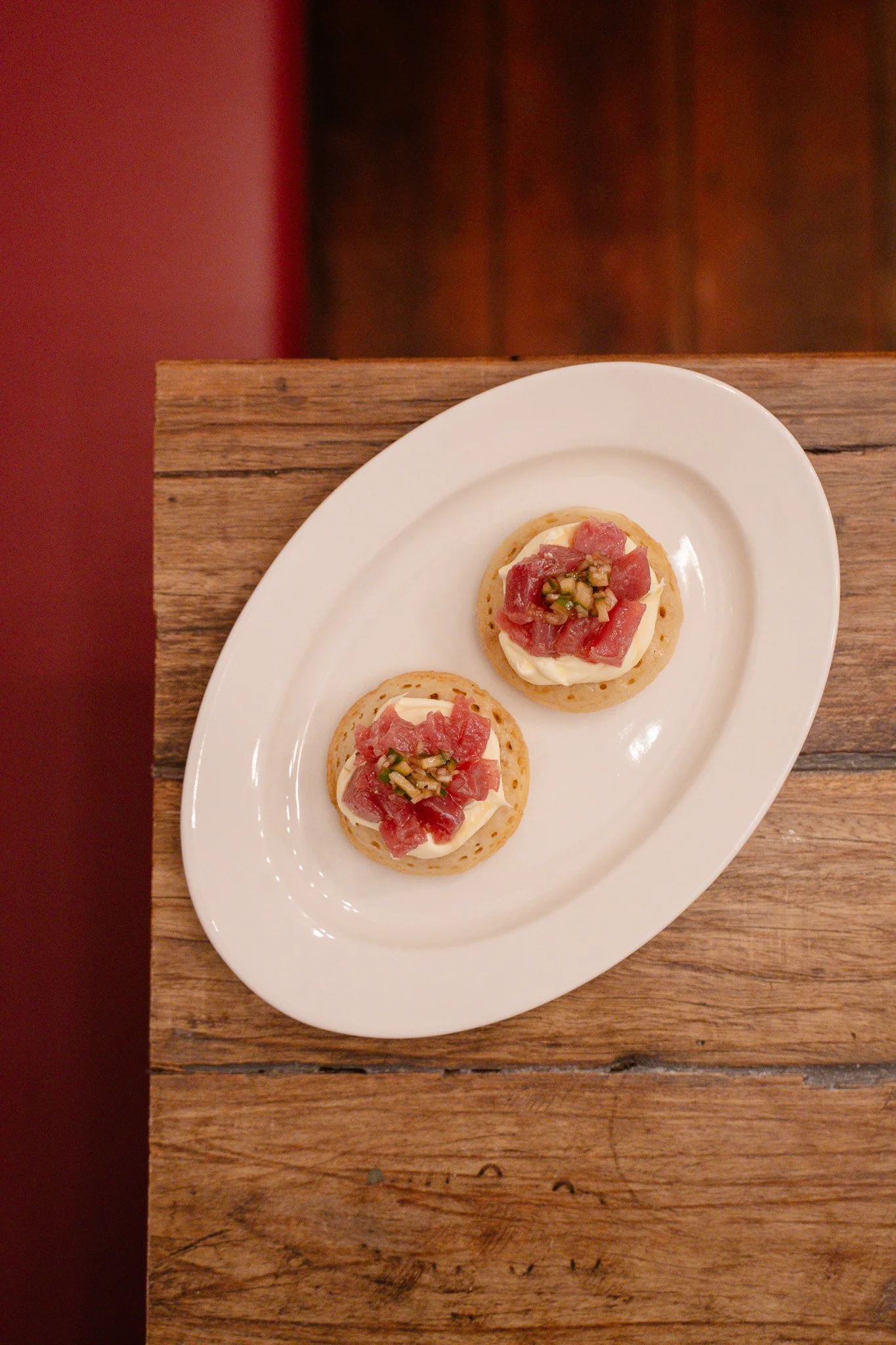 Two canapés with cream cheese, sliced cured meat, and chopped green garnish on a white oval plate.