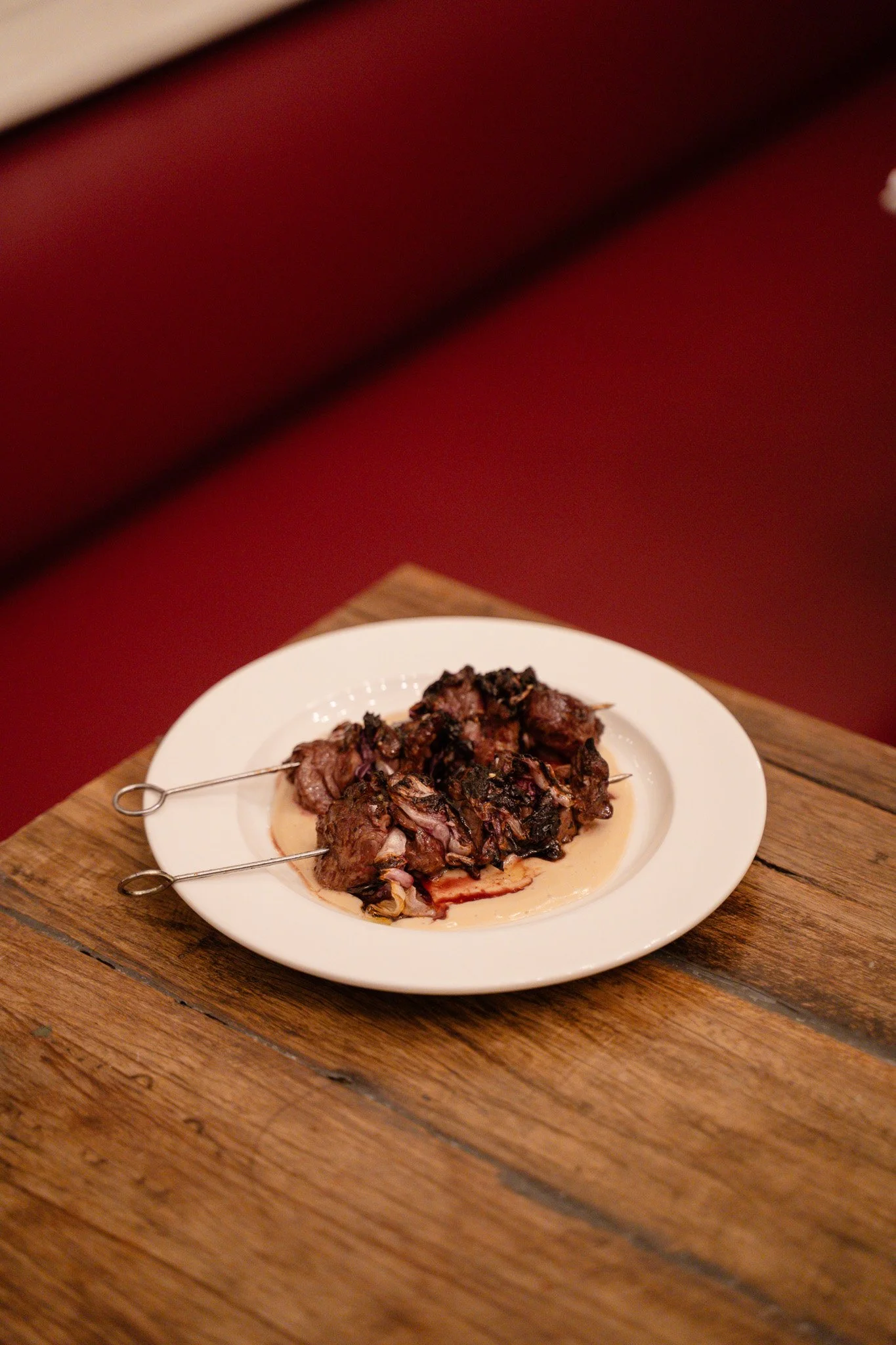 Cooked meat served on a white plate with skewers, placed on a wooden table.