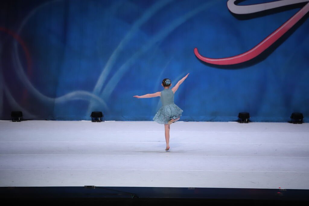 A young girl performing a ballet dance on stage with a blue artistic backdrop.