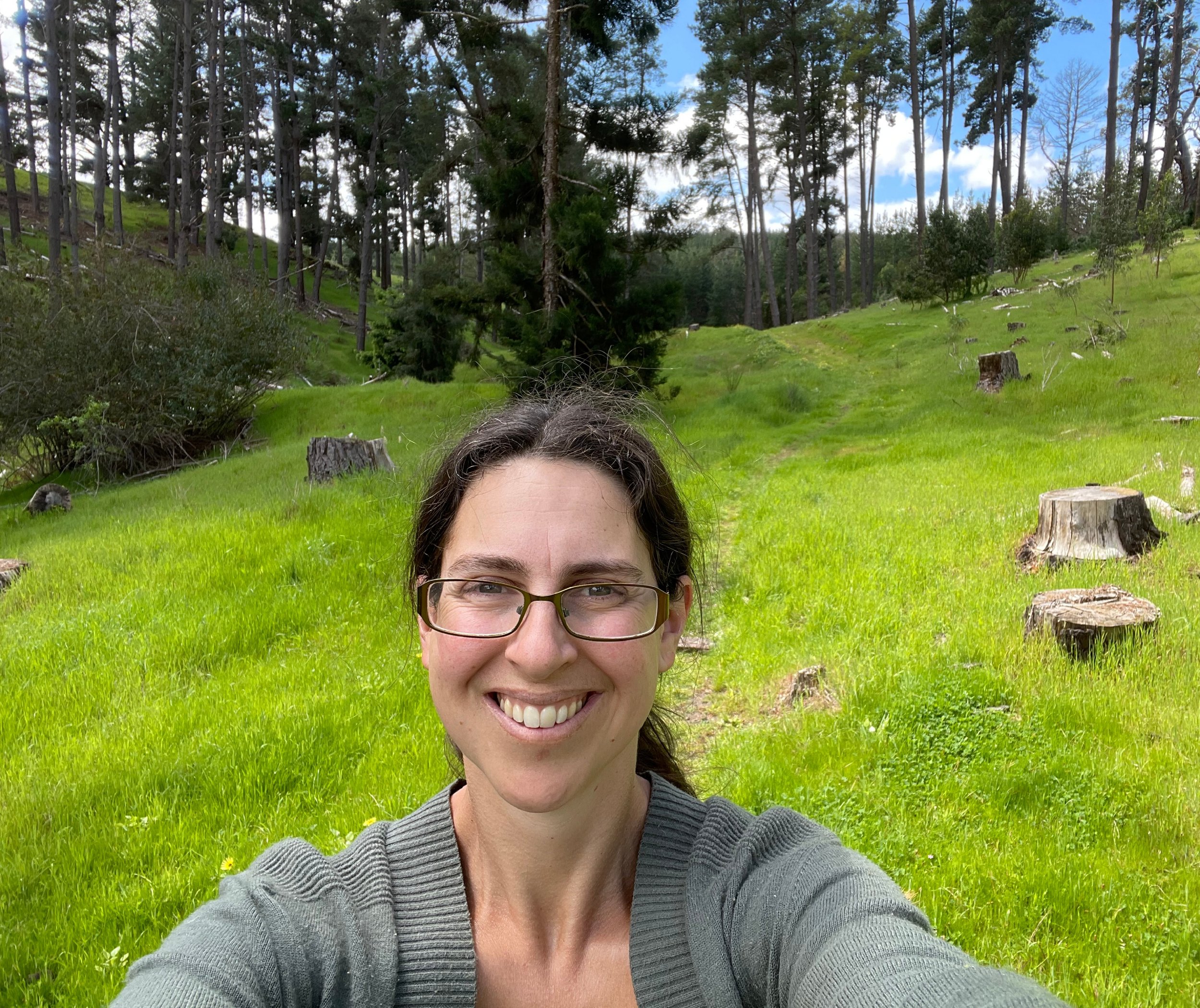 Photo of the author smiling at the camera in a meadow with trees
