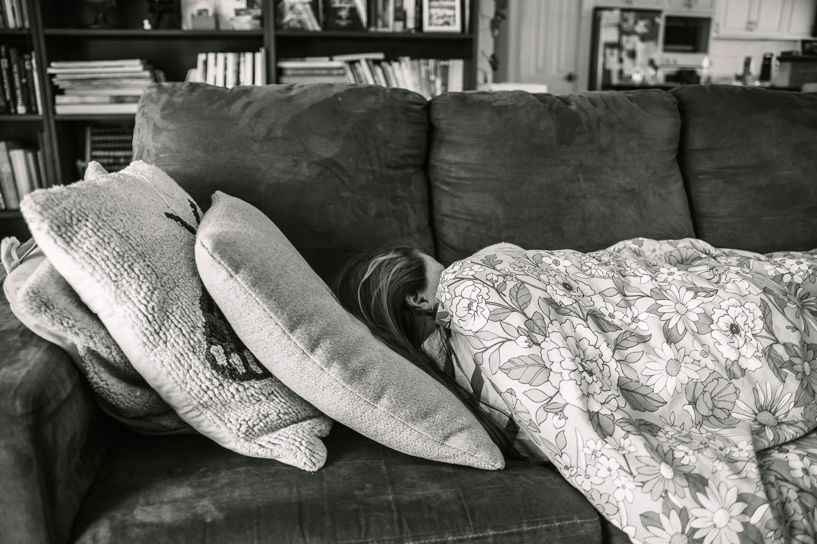 a black and white photo of a girl lying sick on a couch with pillows and blanket around her