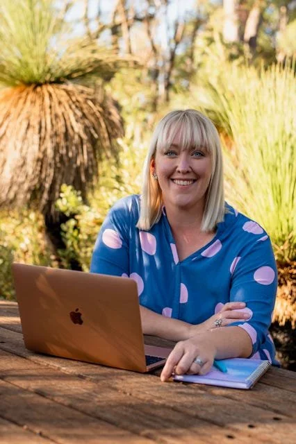 Photo of the author sitting at a table with her laptop in the bush